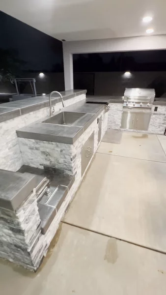 Outdoor kitchen with stone veneer, sink, grill, fridge & concrete fire pit table with bar seating