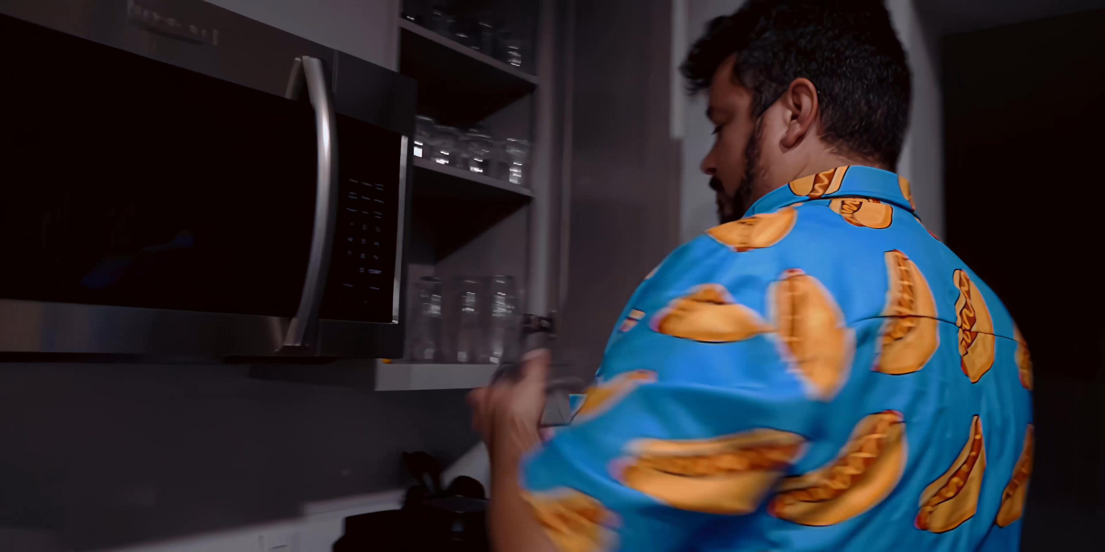 A man in a casual patterned shirt retrieves items from his kitchen refrigerator and pours a drink into a glass. He subsequently examines a bottle of liquor, signaling the transition into a quiet evening at home.