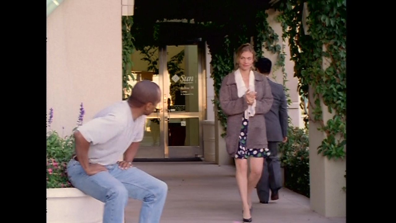 A man sits waiting on a patio before being joined by a woman, with whom he initiates a conversation. The pair then walks together away from the building along a sidewalk.