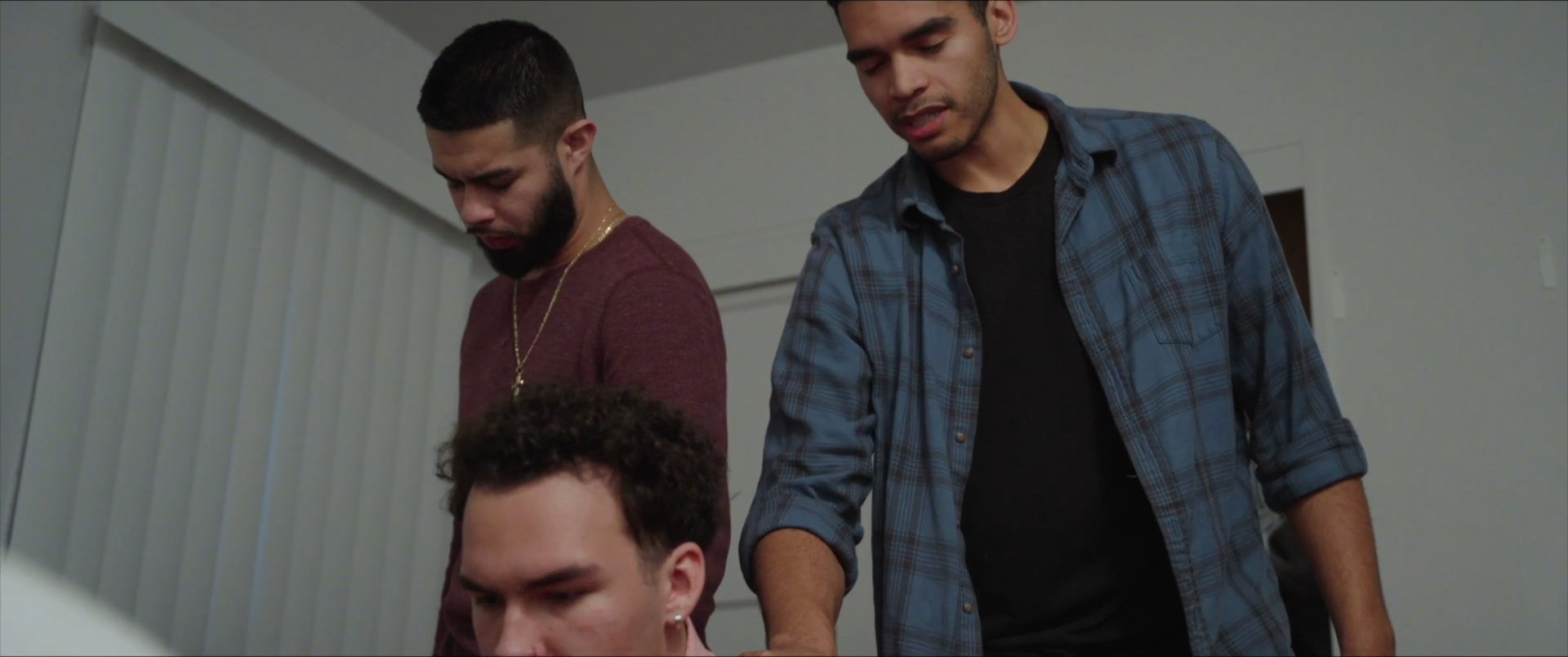 Three men engage in a focused discussion within a residential interior. The participants exchange viewpoints while maintaining an attentive and conversational demeanor.