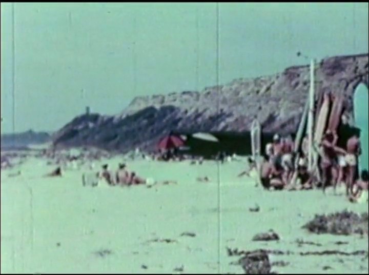Surfers navigate large waves before transitioning to a vibrant beachside gathering featuring vintage automobiles, social activities, and traditional hula performances.