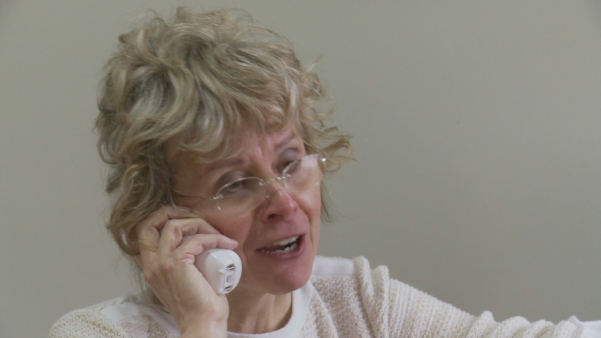 A man and a woman navigate an emotional moment while separated, with the man clutching a stuffed animal in a living room as the woman speaks on the phone.
