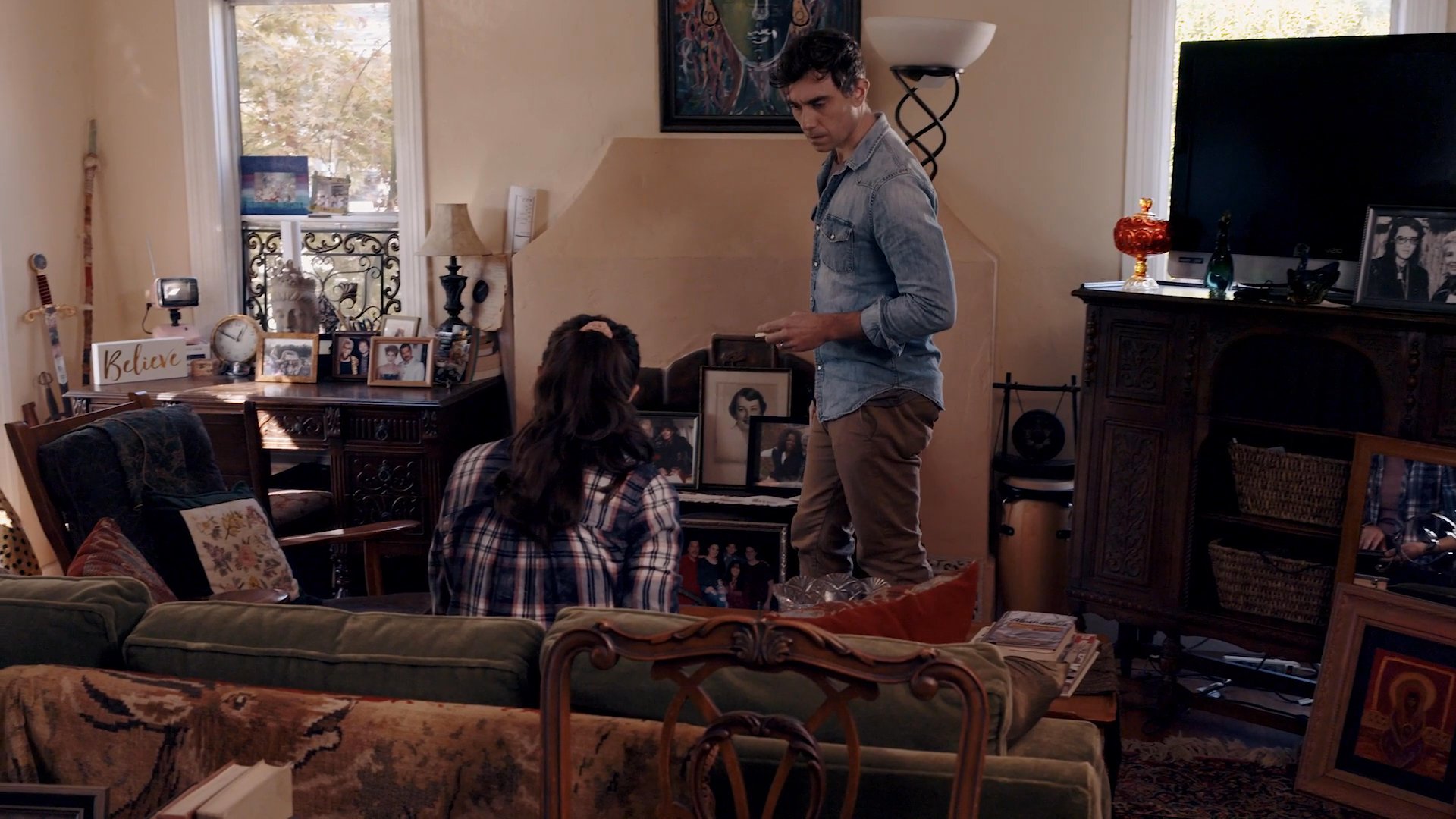 A man and woman revisit memories while looking through a photo album together in their living room. Their quiet interaction highlights a moment of personal reflection and connection.