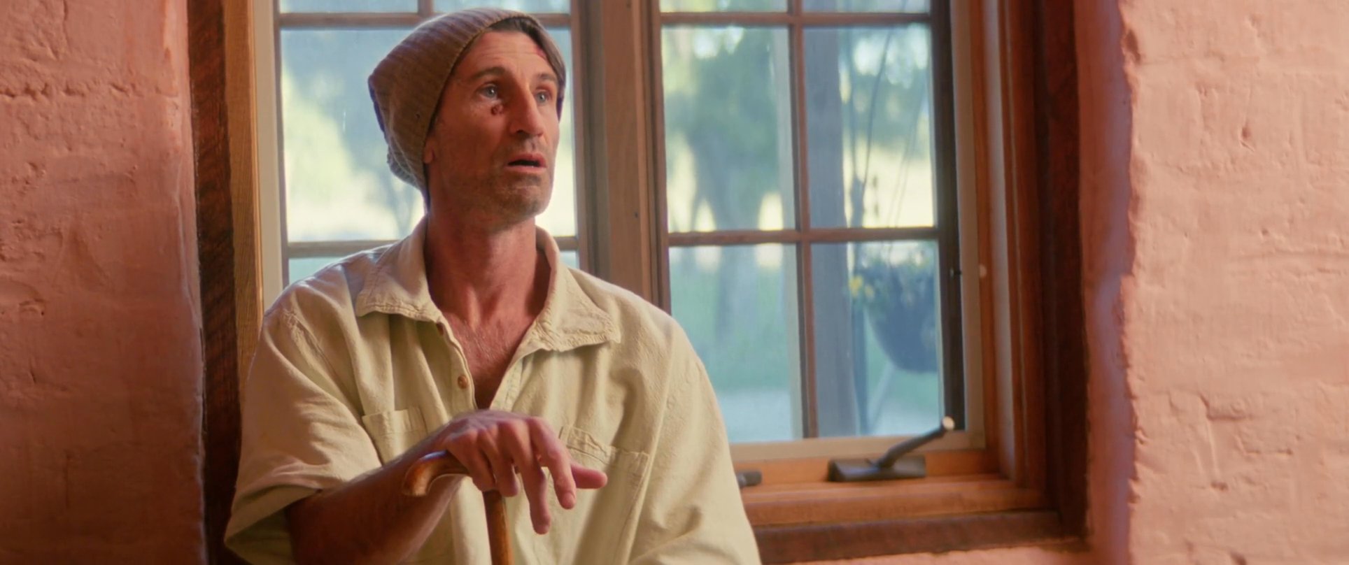 Two men engage in a tense conversation within a room featuring warm-toned walls and window lighting. The scene shifts between the individuals as they exchange dialogue, capturing their focused expressions and physical mannerisms.
