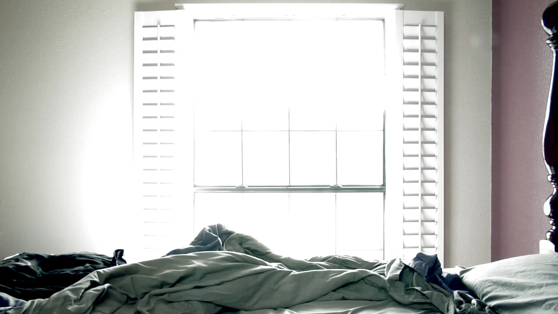 A man exhibits signs of distress and deep reflection while sitting alone in a bedroom. His demeanor fluctuates between sorrowful prayer and somber introspection.