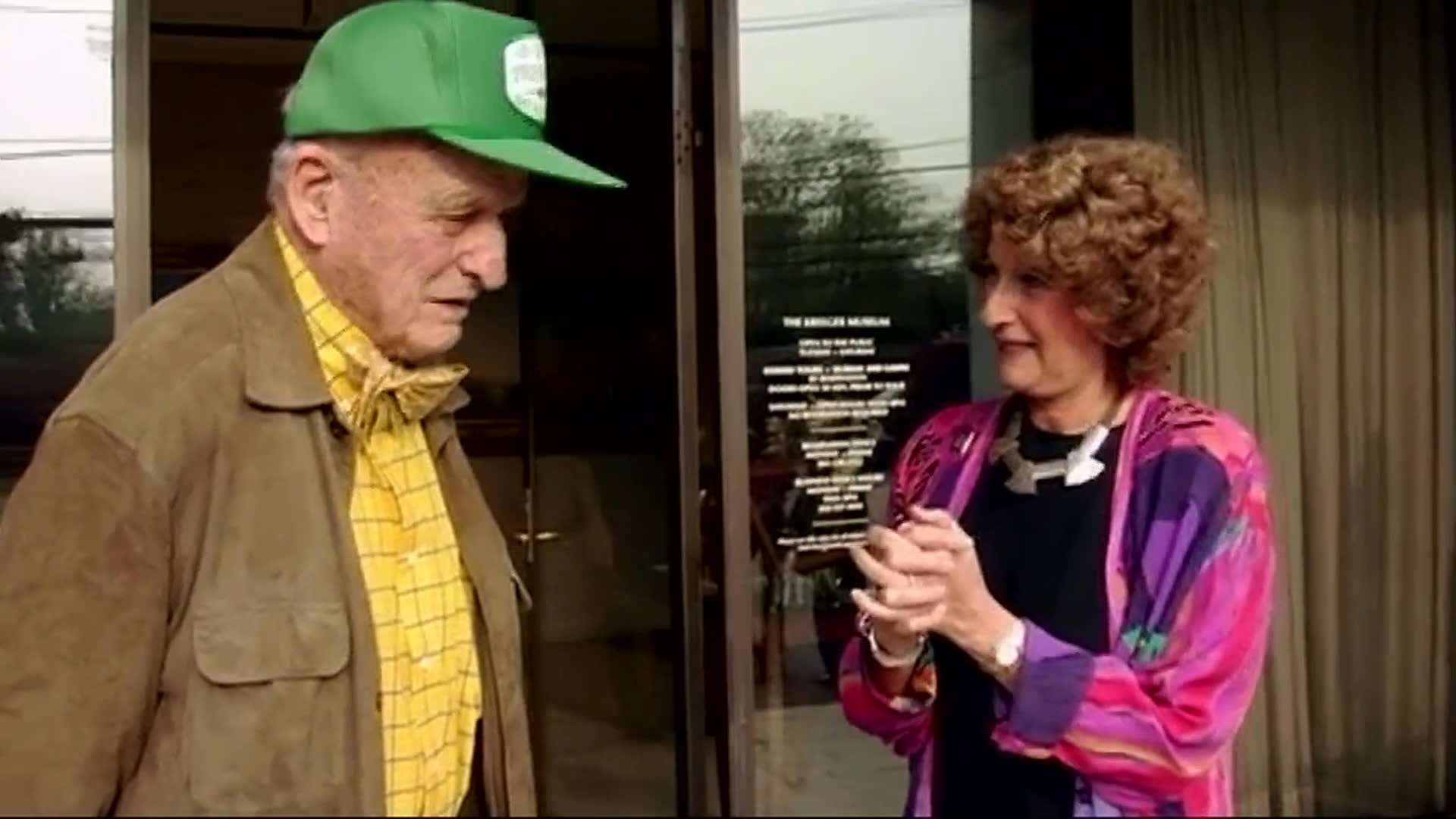 Judy Greenberg speaks with an older man outside the Kreeger Museum, sharing a light conversation beside the entrance. They move indoors as their exchange continues.