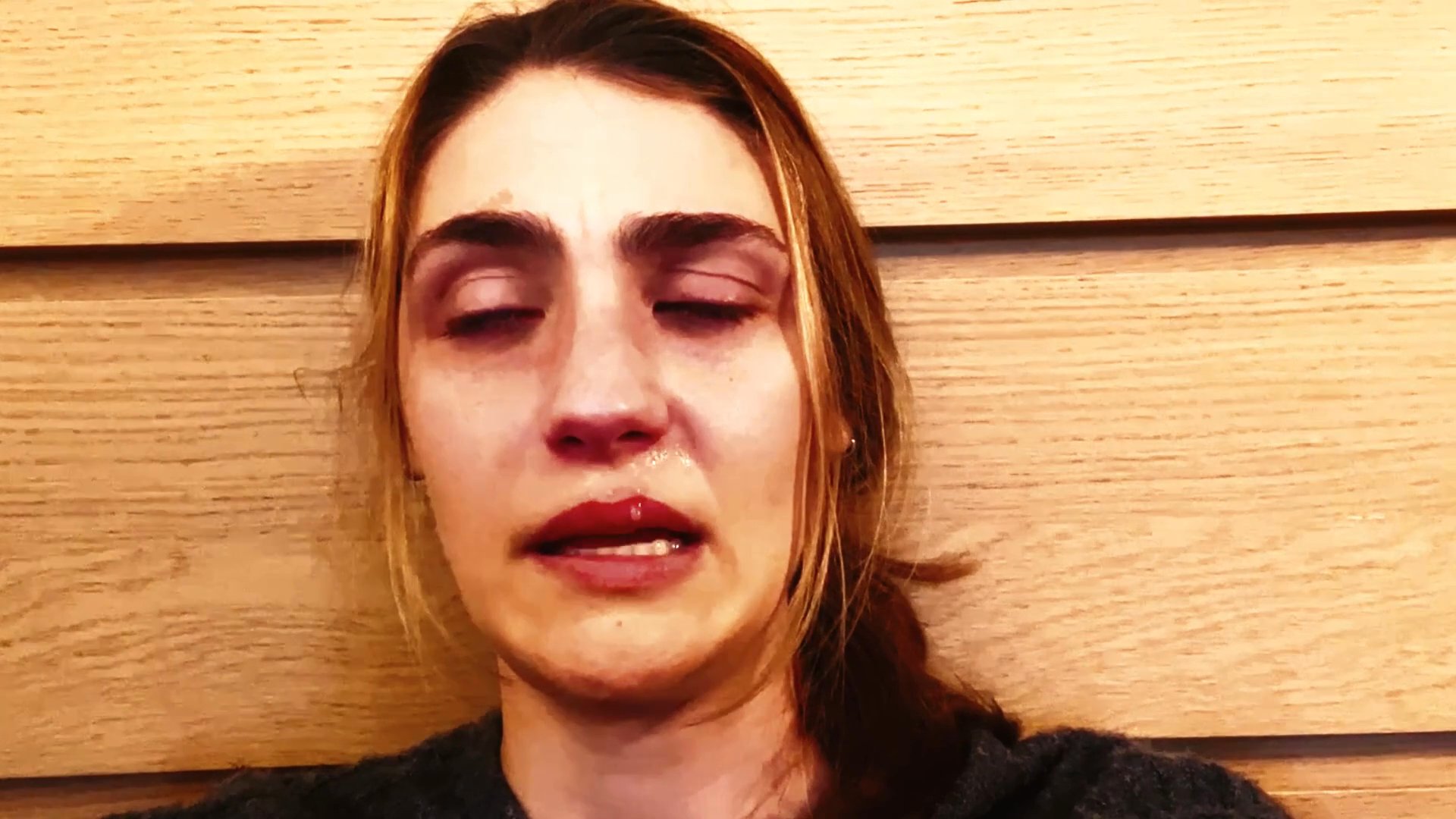 A woman with visible tears and reddened eyes displays a sequence of intense, sorrowful expressions against a wooden background. Her changing facial features convey a deep sense of vulnerability and emotional turmoil.