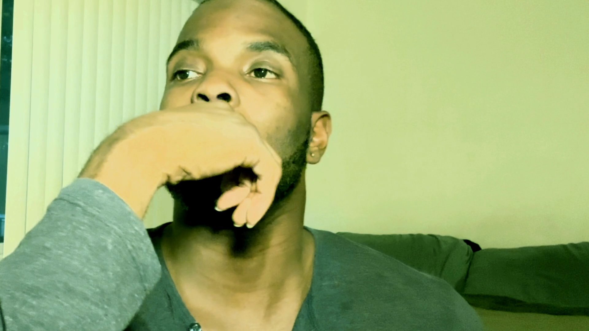 A man with a beard sits indoors, resting his hand against his face while displaying a deep, contemplative expression.