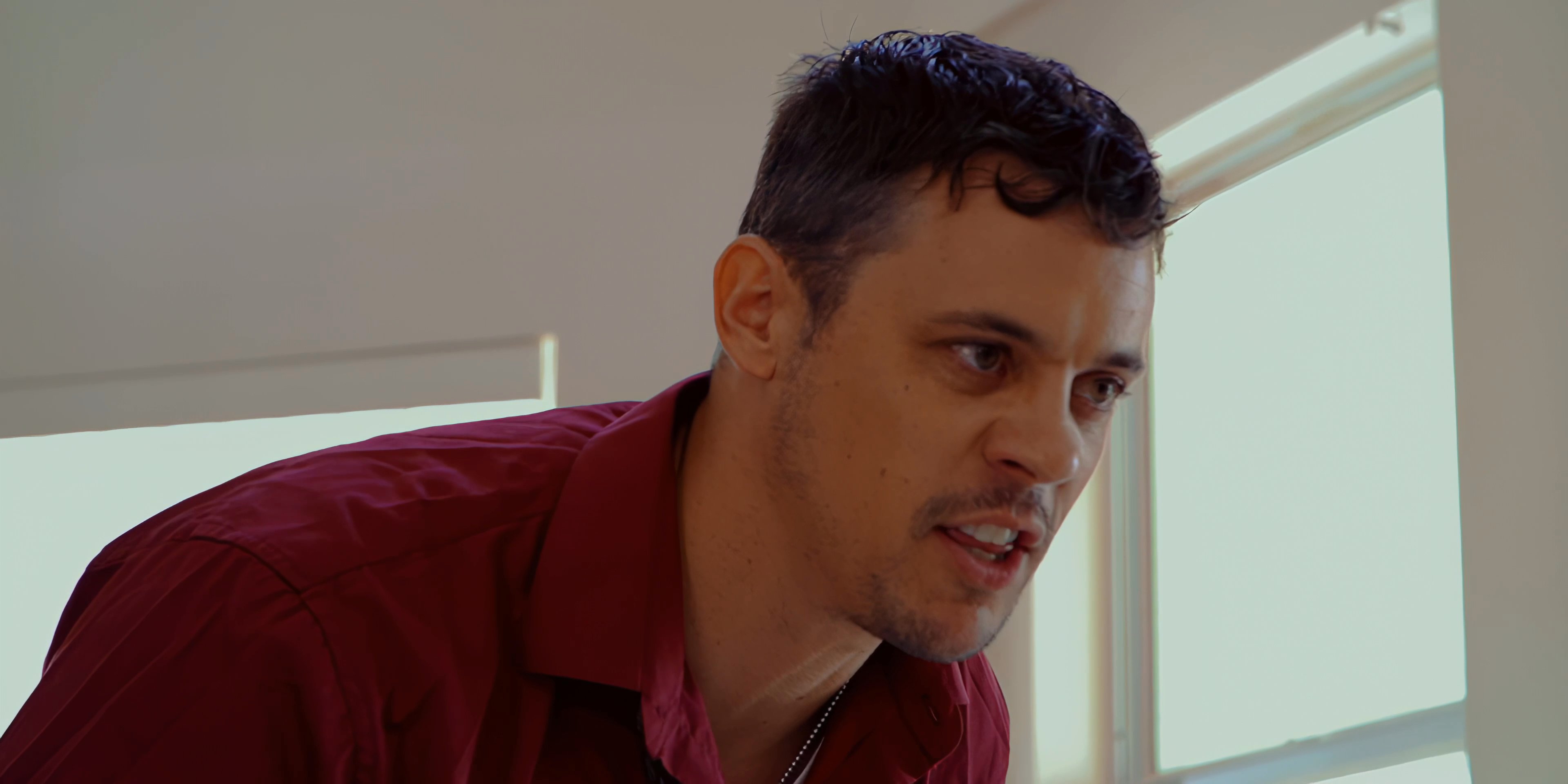 Two men engage in an emotionally charged argument within an indoor setting, with one individual leaning in aggressively while the other responds defensively from a seated position.