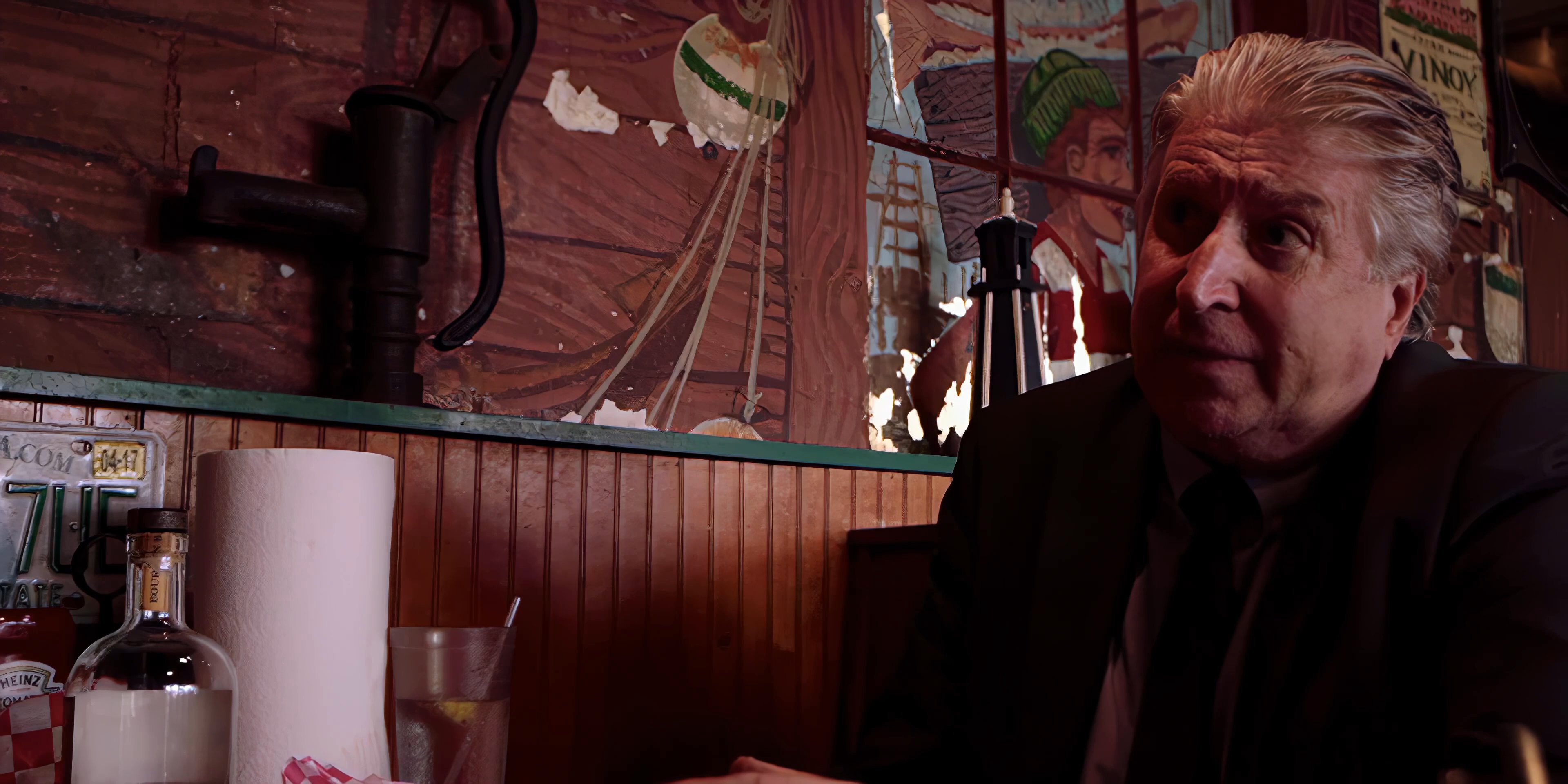 Two men engage in a serious, focused conversation while seated in a diner booth. The individuals gesture and maintain active eye contact throughout their interaction.