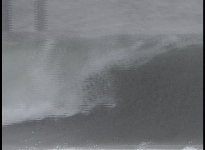 A surfer maneuvers through powerful waves near a busy beach and pier, followed by shots of the surrounding coastline and a lighthouse.