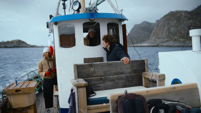 Two women and one man on a wooden boat rocking back and forth on the sea