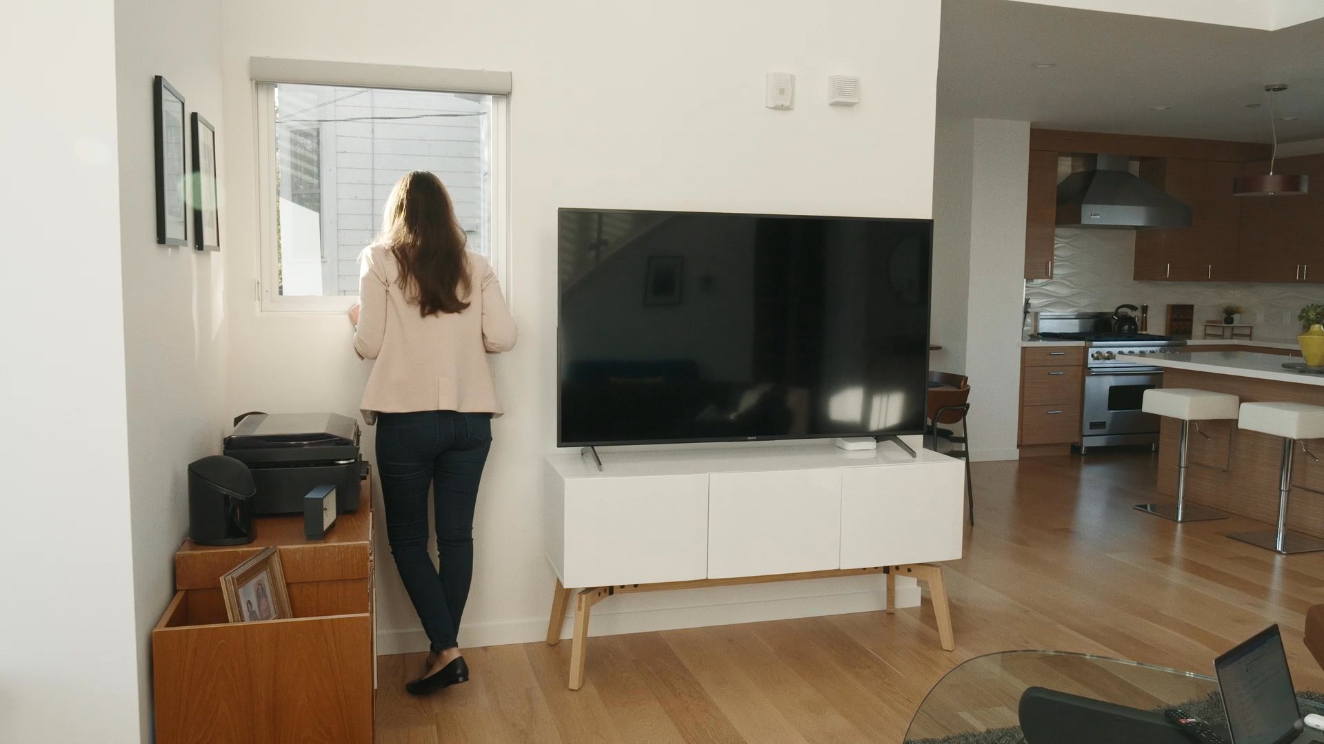 A man walks through an outdoor parking lot while a woman arrives home and enters her living space, signaling the transition between public and private environments.