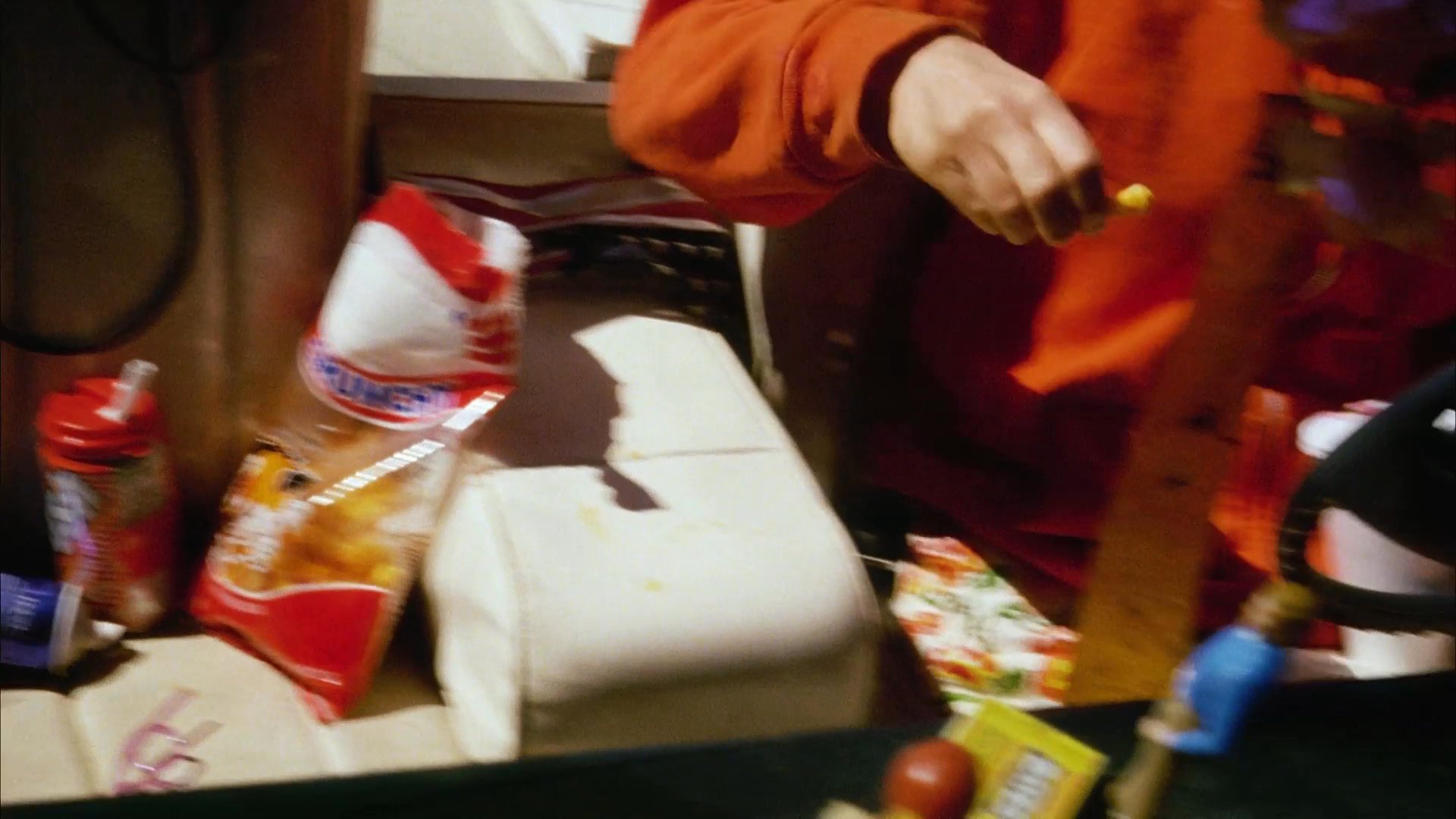 A woman eats fast food in the passenger seat of a car parked near a grassy wetland. The interior environment includes small toy figures on the dashboard as the vehicle sits idle.