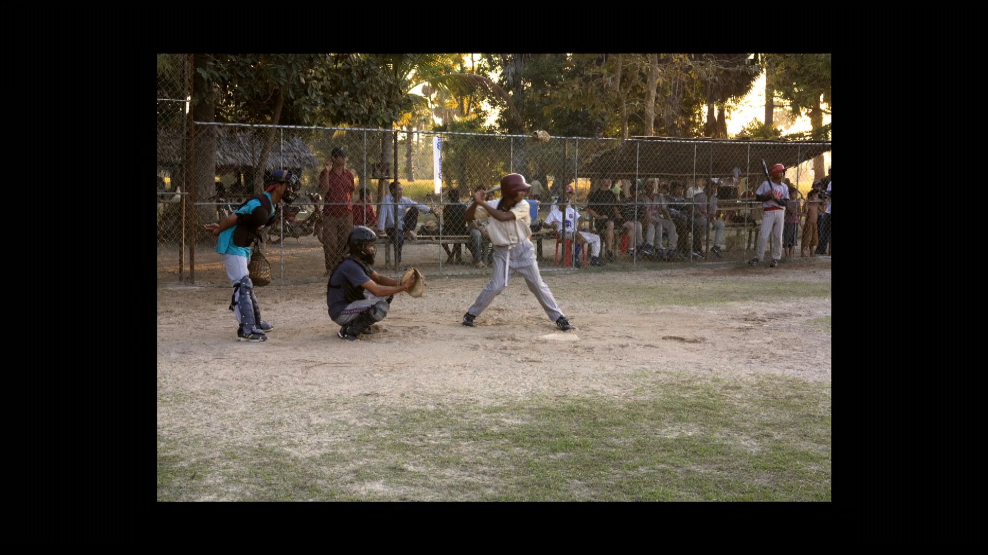 Young athletes participate in a baseball practice session led by adult coaches on an outdoor dirt field. The training focuses on fundamental skills and team coordination in a rural community environment.