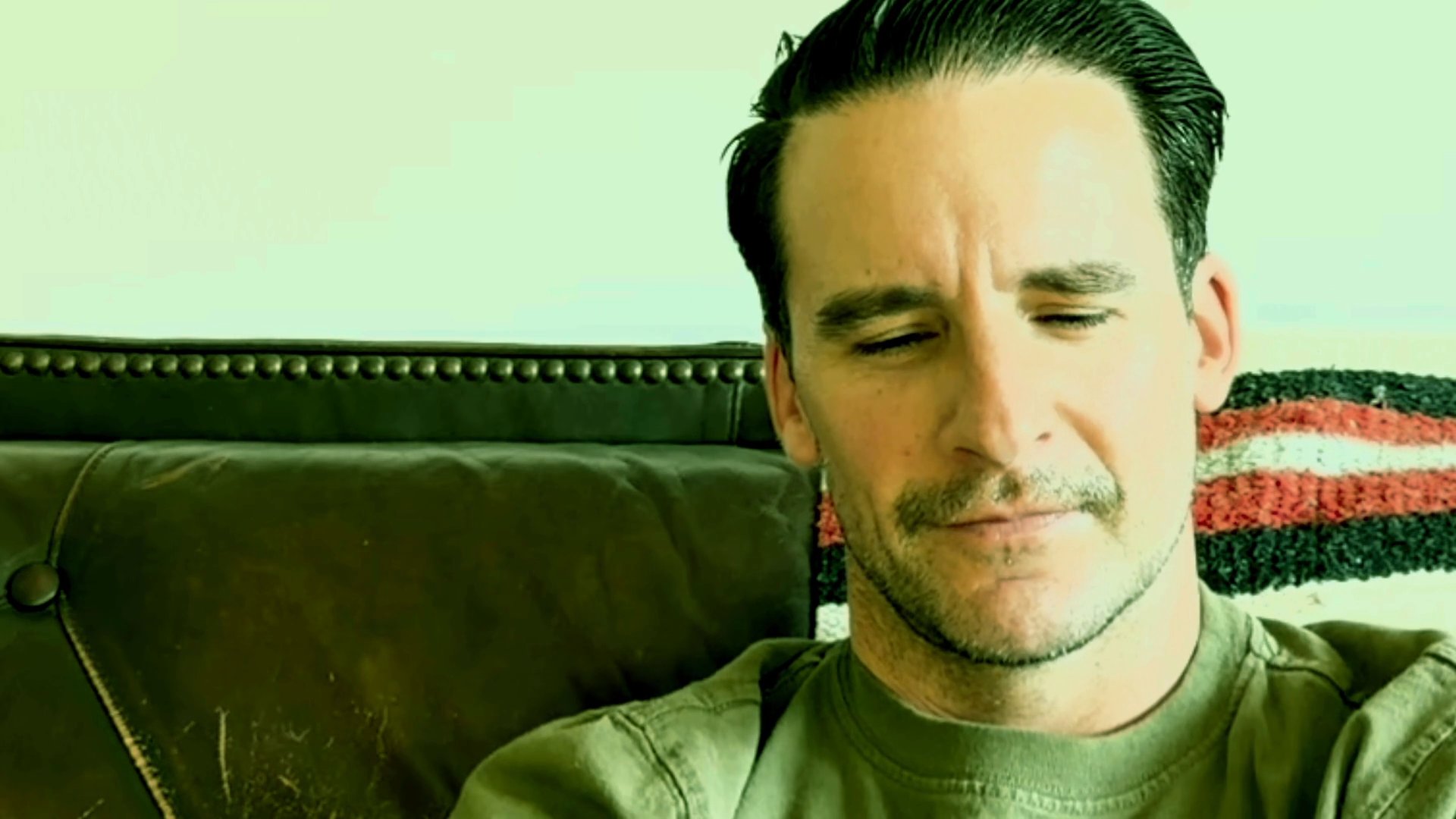 A man sits on a sofa, conveying thoughts through subtle changes in expression and steady, focused engagement while speaking.