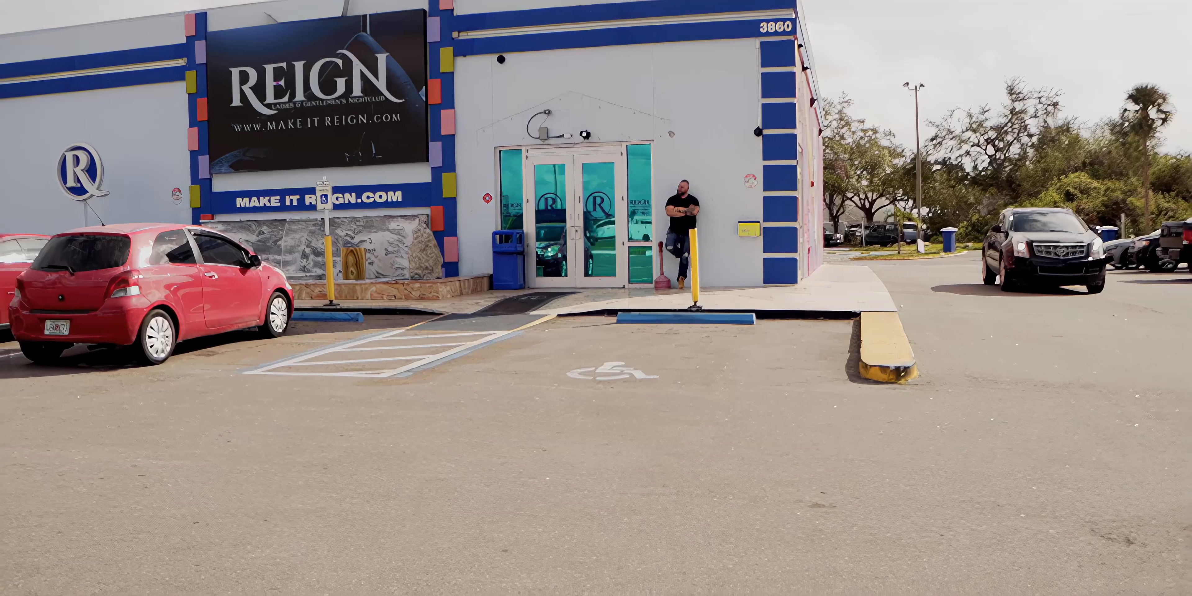 A man stands outside a commercial building and observes vehicles arriving in the parking lot. The sequence transitions from wide environmental shots to a focused portrait of the individual.