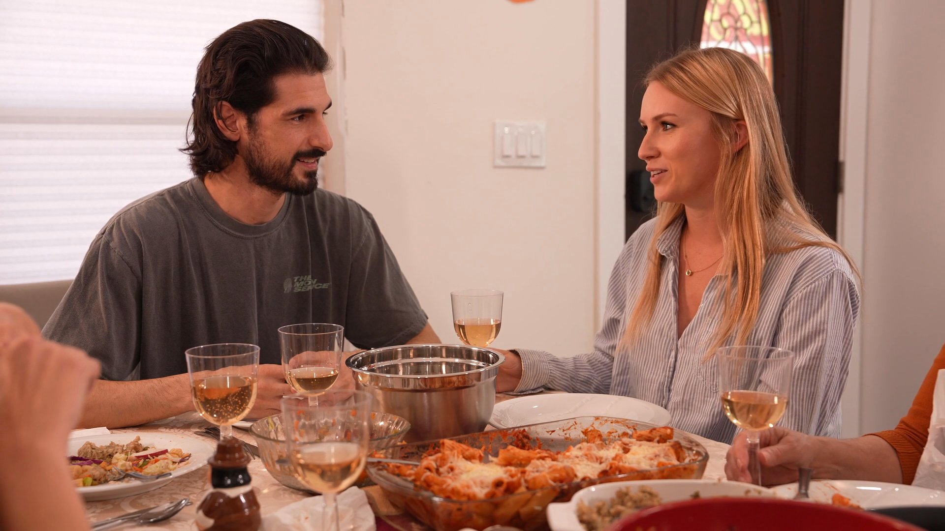 A man and a woman engage in pleasant conversation while sitting together at a dinner table. They share a meal and drinks in a comfortable, domestic environment.