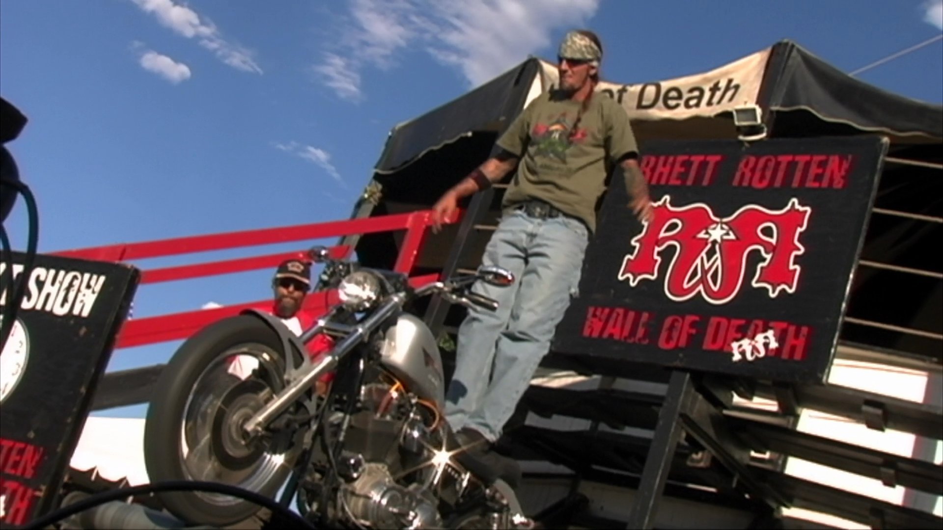 A motorcycle stunt performer demonstrates gravity-defying maneuvers on the Wall of Death, transitioning from an energetic outdoor festival setting to a high-speed arena performance.