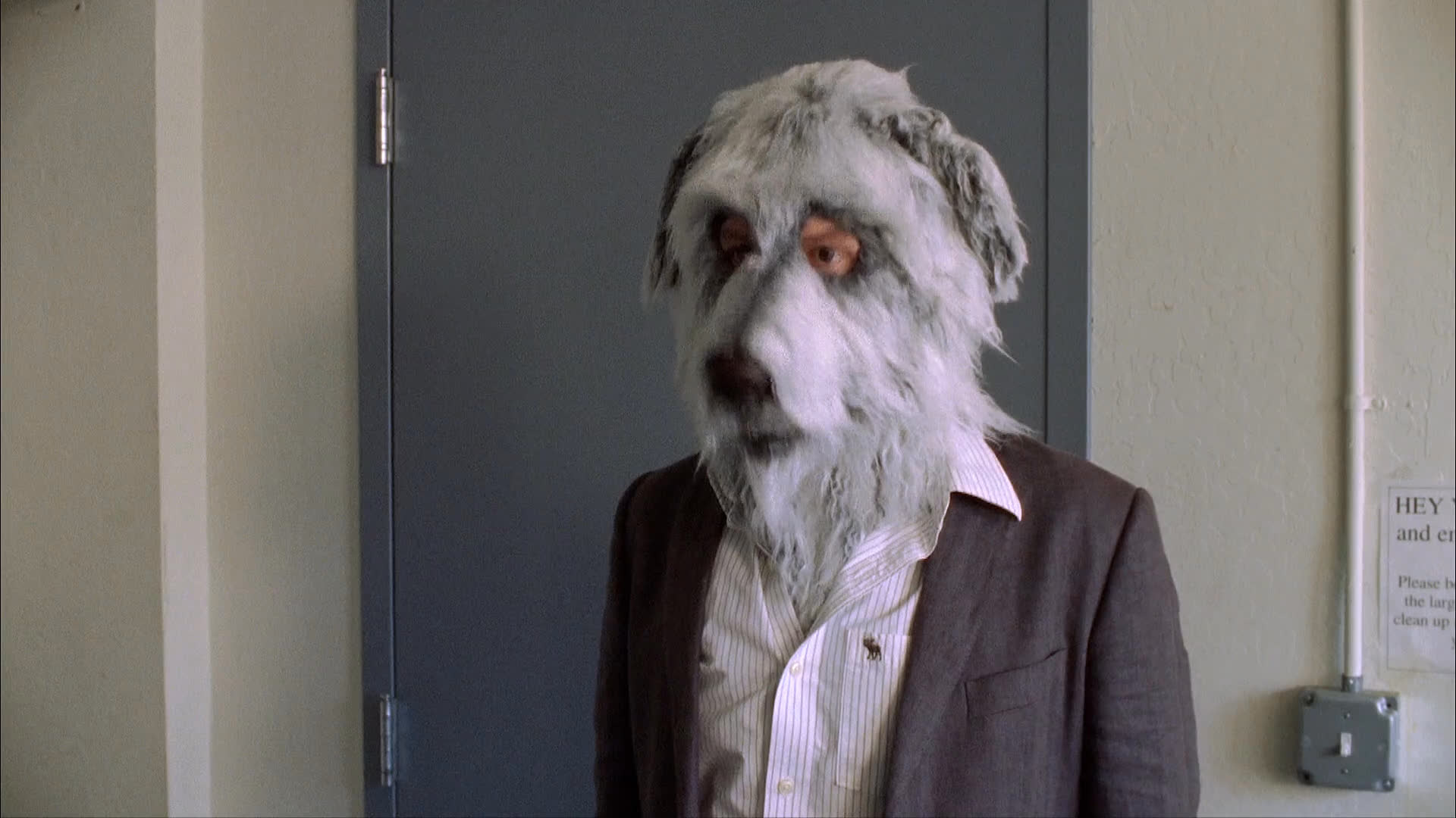 An actor wearing a realistic dog mask practices for a performance, alternating between his human persona and the character-driven costume within a studio setting.