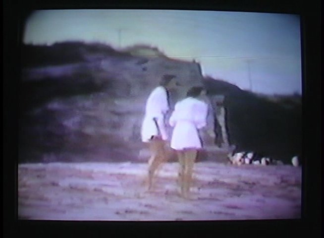Historical film captures women walking along a beach, interspersed with a modern-day interview reflecting on the archival footage.