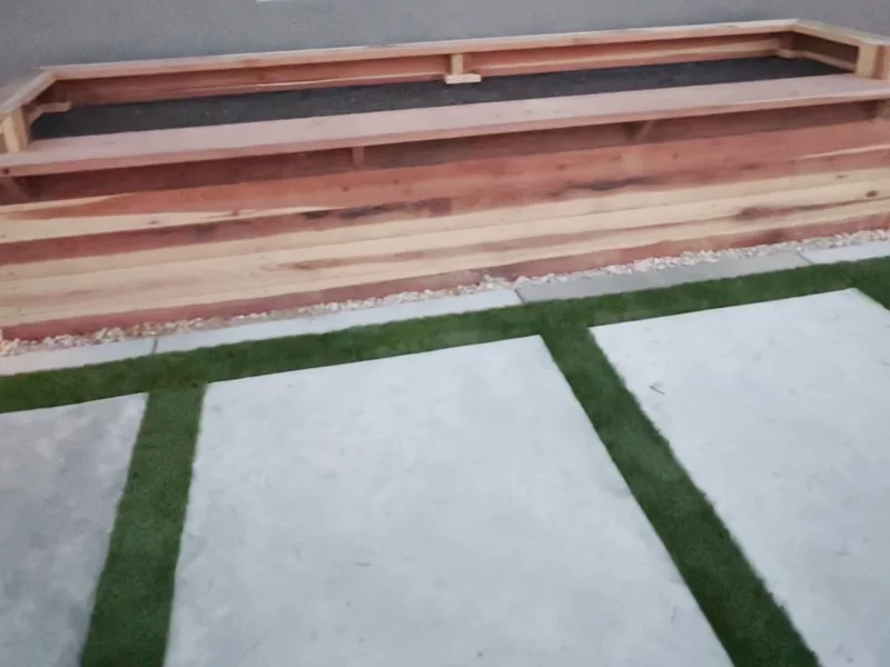 Artificial turf with modern concrete pavers featuring a wooden raised planter box