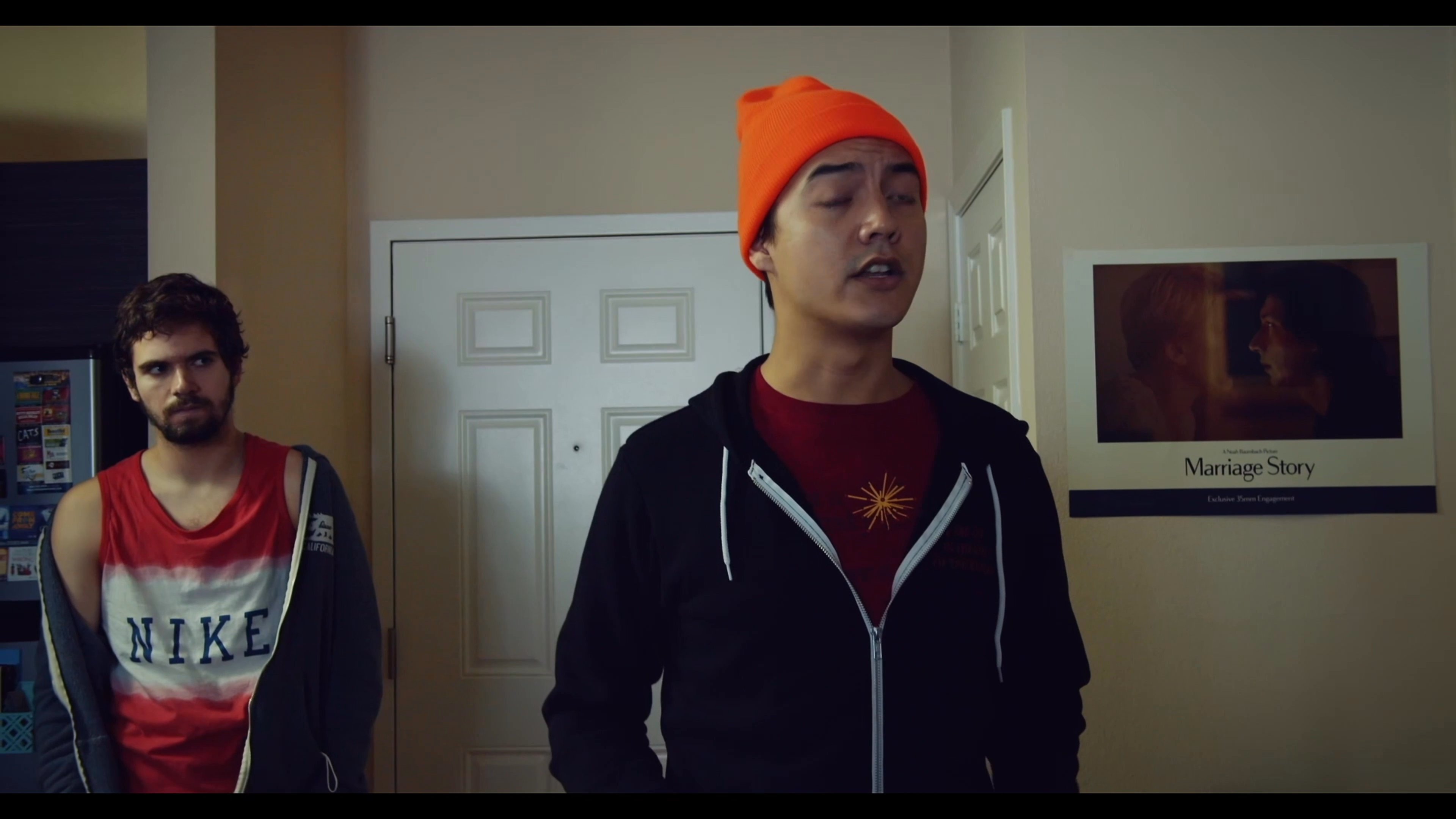Three young men engage in a tense conversation inside a residential living space, with one individual pacing while delivering dialogue to the others.