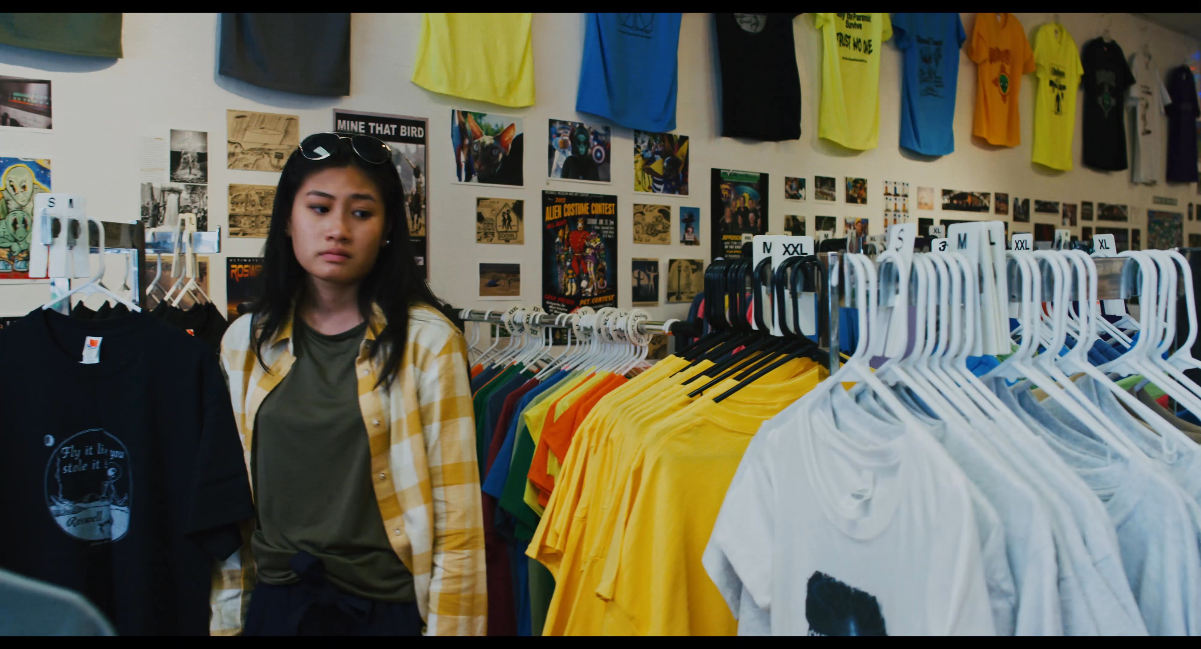 A woman browses through a selection of graphic t-shirts displayed on clothing racks in a retail store.
