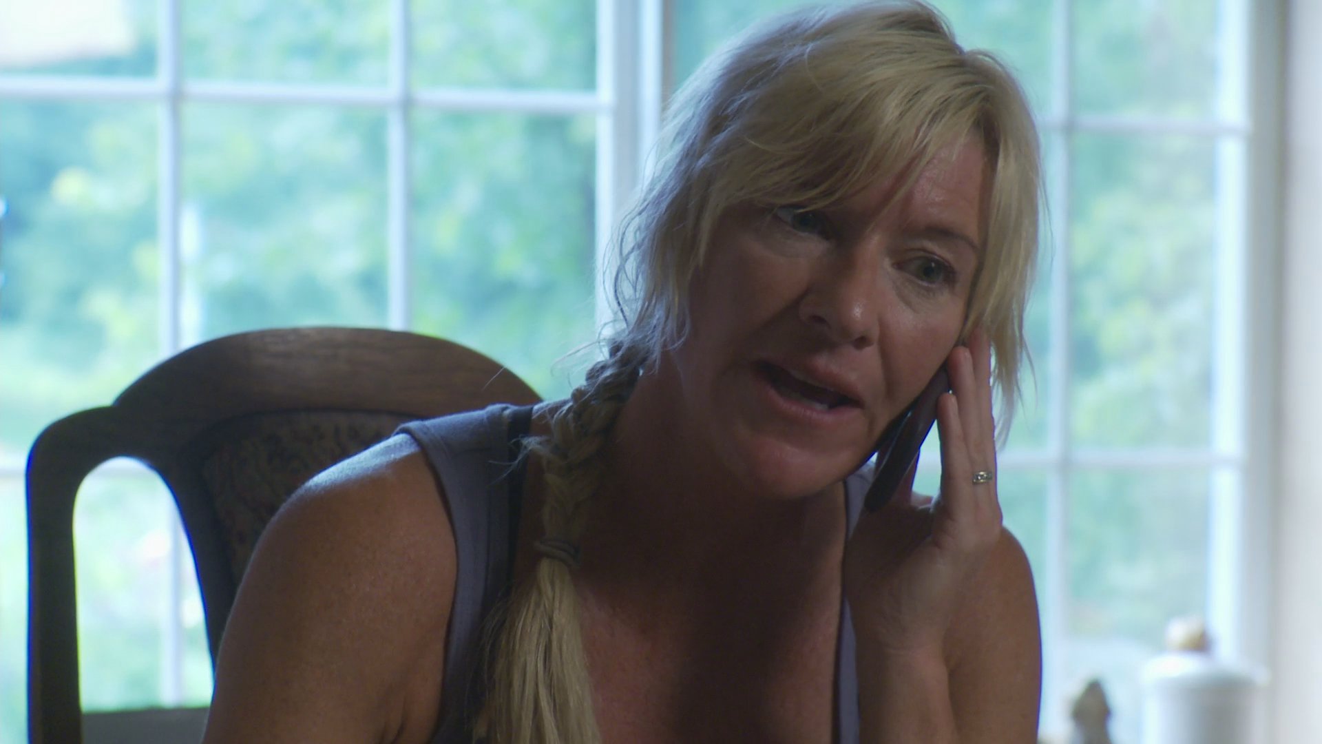 A woman engages in a serious and expressive telephone conversation while seated at an indoor workspace. The dialogue alternates between different individuals, highlighting the ongoing nature of their professional discussion.