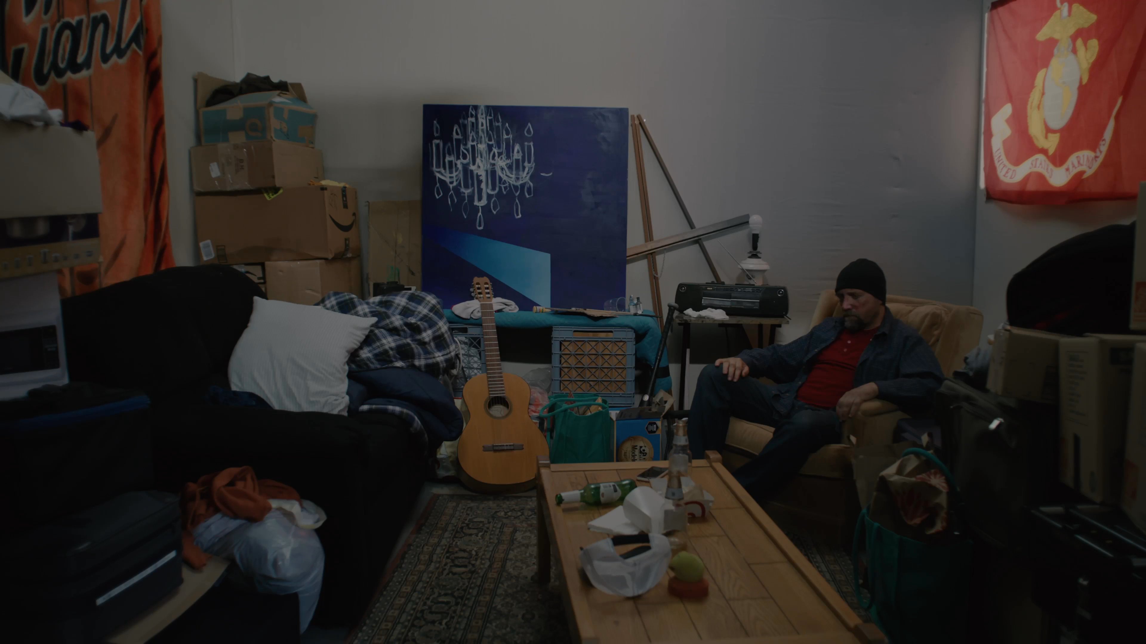 A man sits pensively in a living room chair before another individual enters the frame to engage him in conversation.