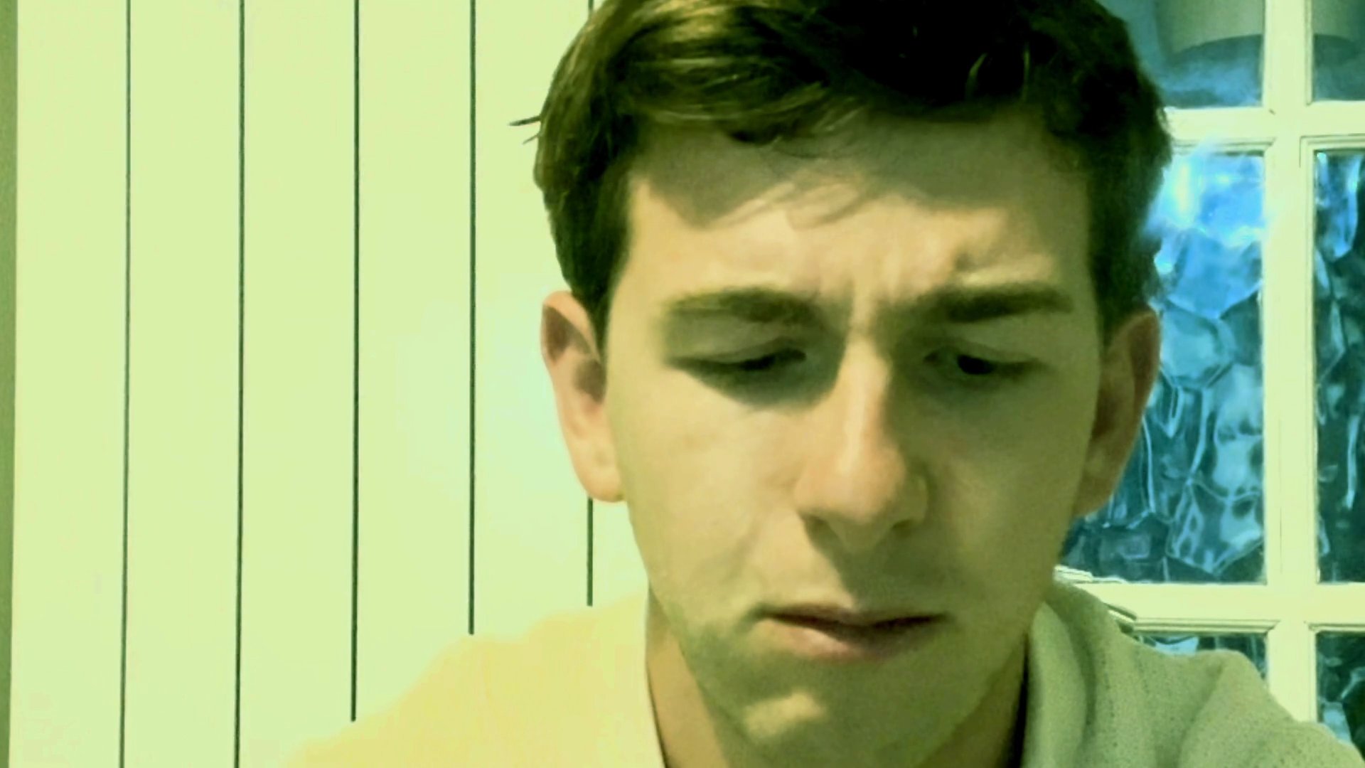 A young man speaks directly to the camera, delivering a focused message in an indoor setting. His facial expressions and tone suggest a deliberate and earnest communication style.