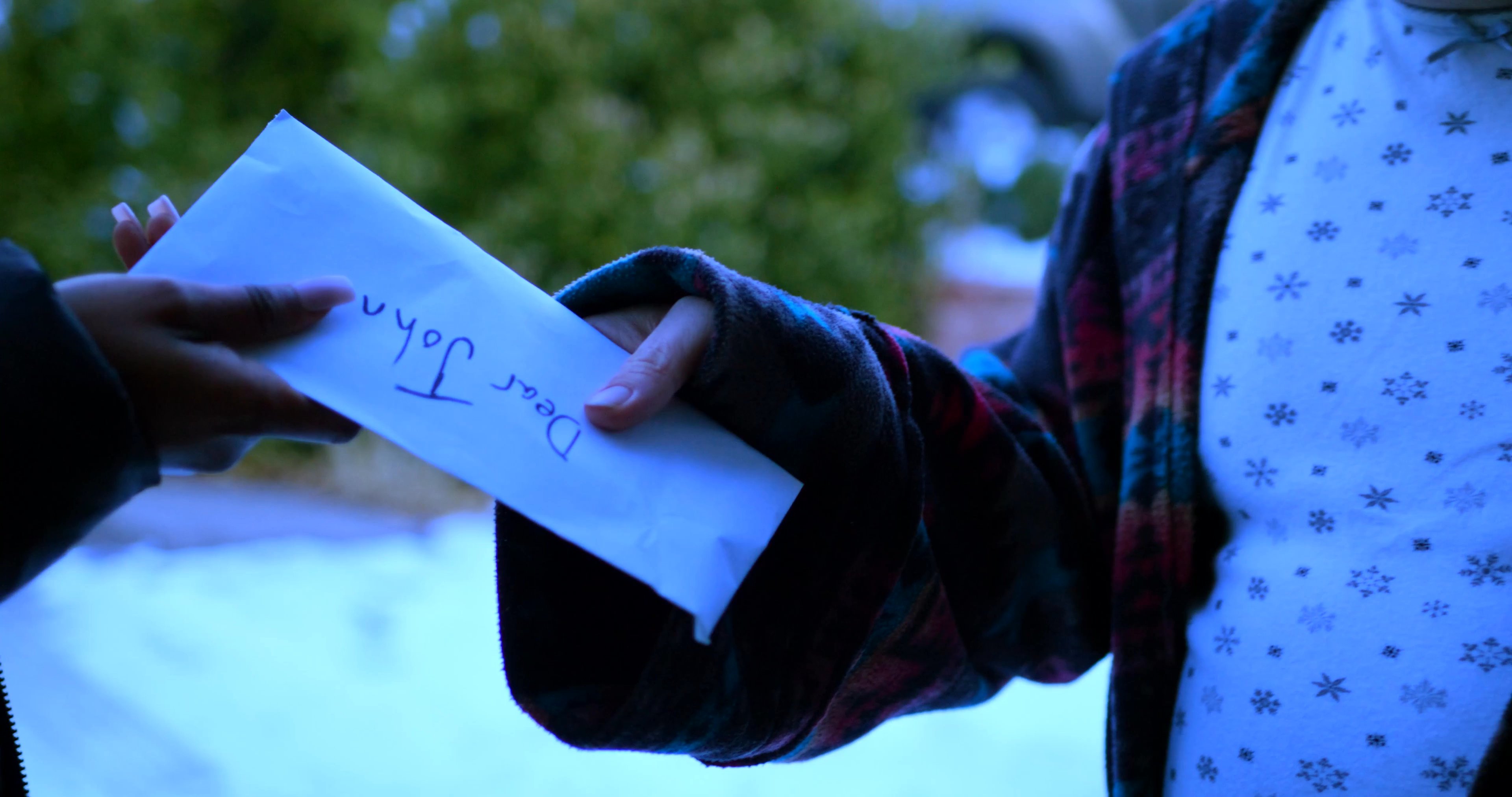 A person delivers a letter to an individual outside a residential home during a winter day. The exchange concludes as the recipient processes the message and the deliverer departs.