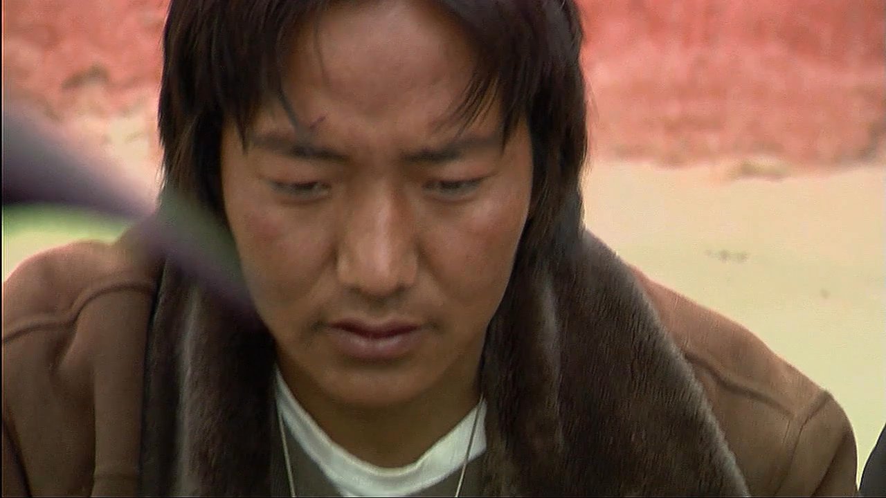 A group of artisans gathers in a Tibetan monastery courtyard to meticulously prepare pigments and paint an intricate, traditional mandala.