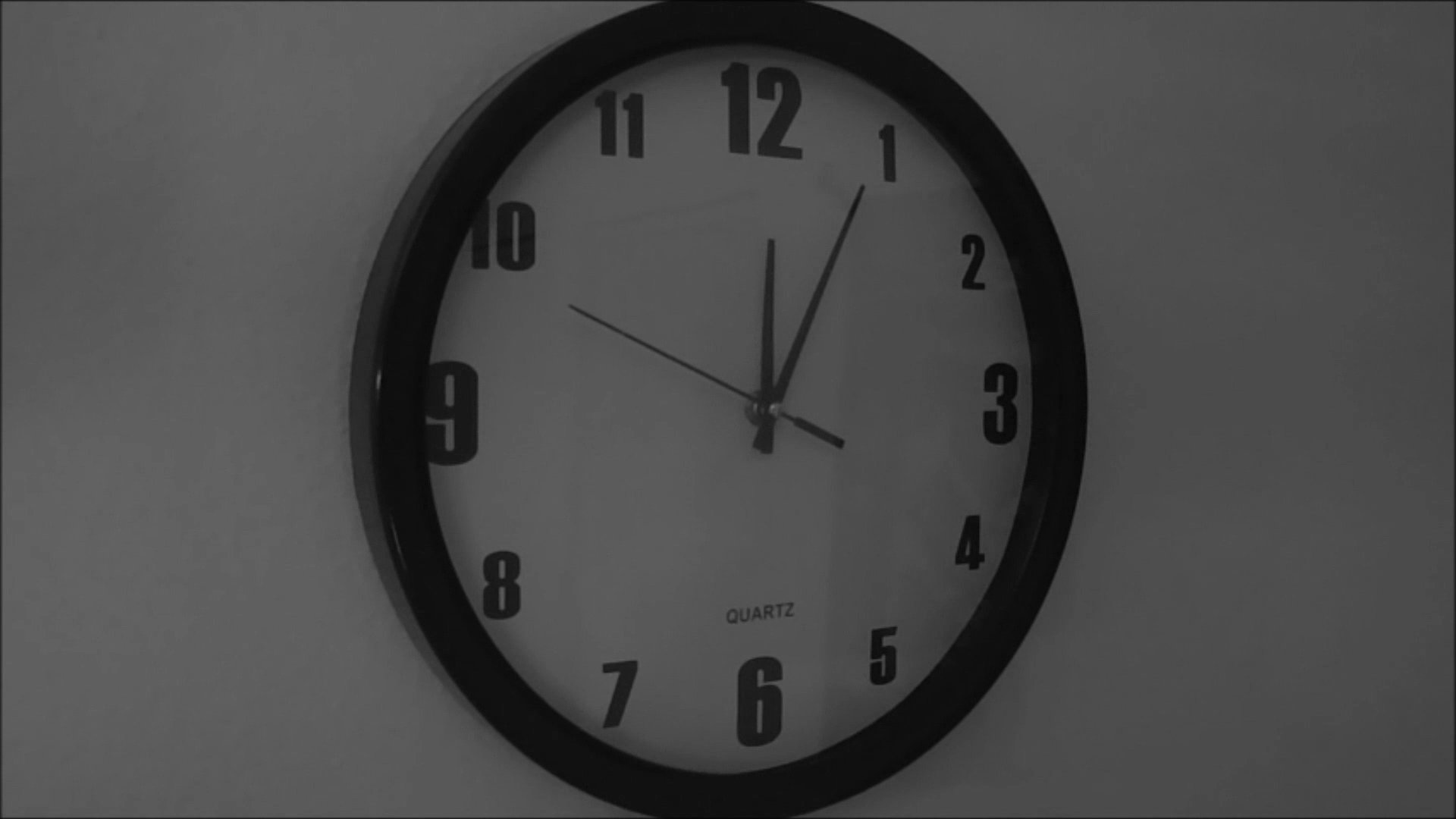 A man sits alone at a dining table, looking toward a clock as he waits, expressing a sense of isolation and anticipation.