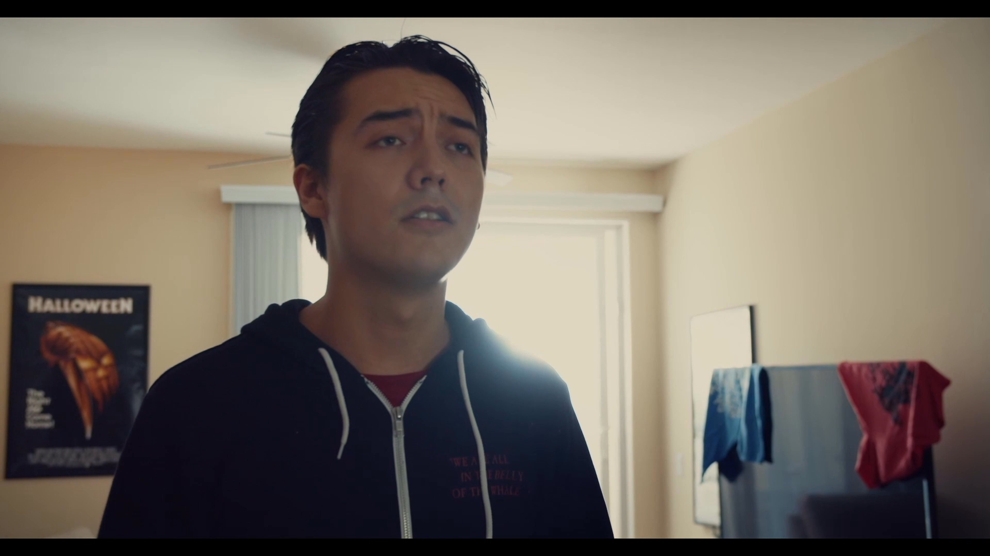 A man reacts to his roommate entering their apartment while carrying a backpack, leading to an immediate verbal interaction between them in the living space.