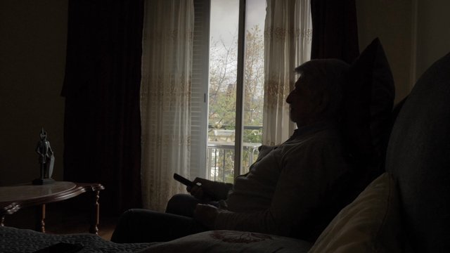 An old man sitting on a couch and changing the TV channel