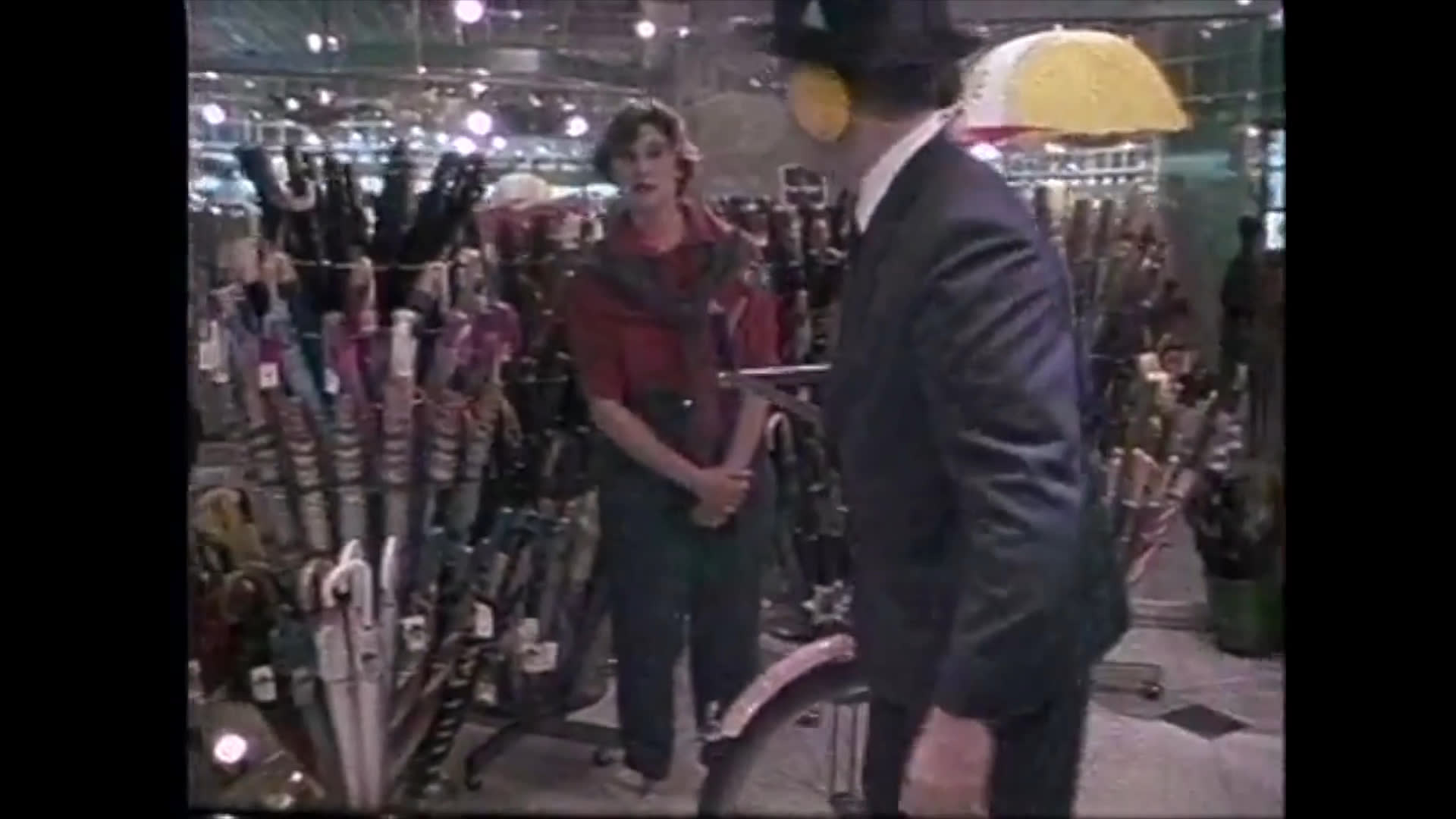 A customer interacts with a sales associate in a retail store specializing in umbrellas. The customer selects, tries on, and examines a product while the associate assists with the process.