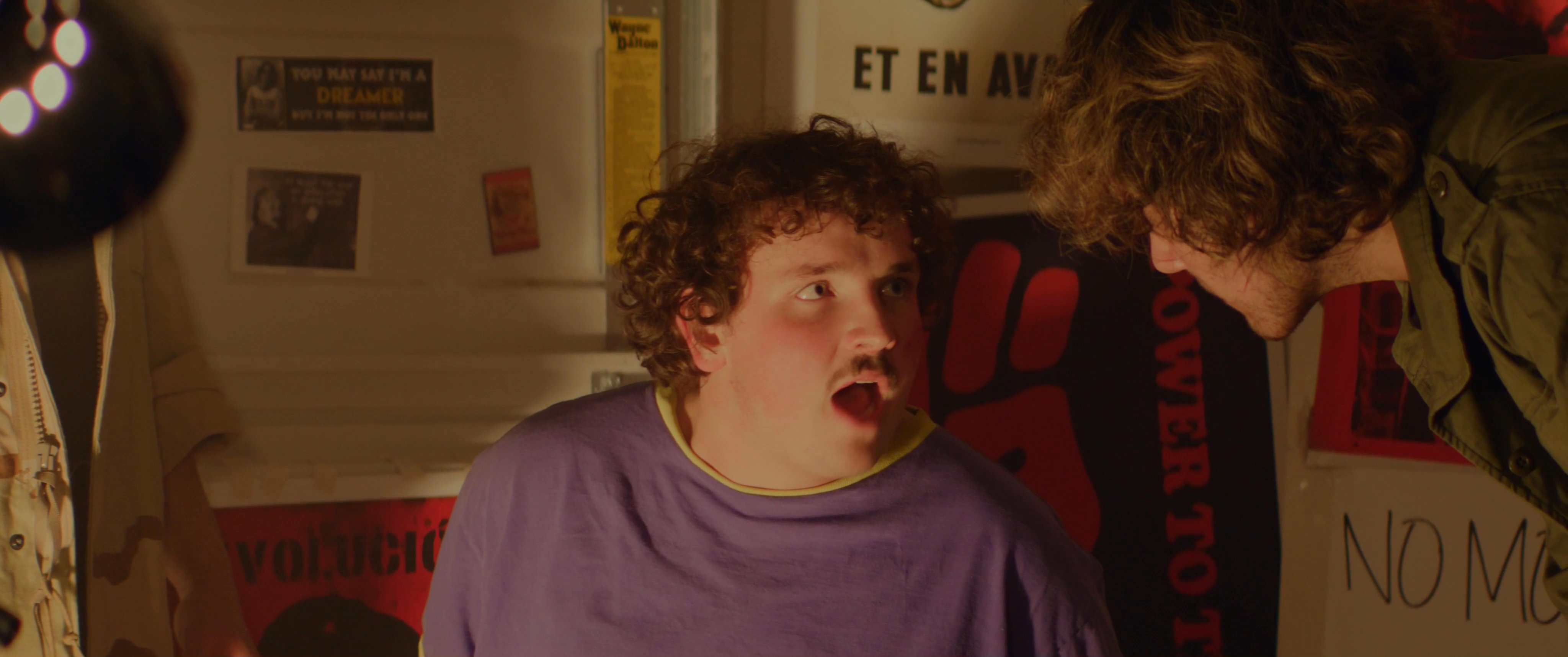 Two actors engage in an intense, animated conversation while rehearsing a scene in an indoor space decorated with posters.