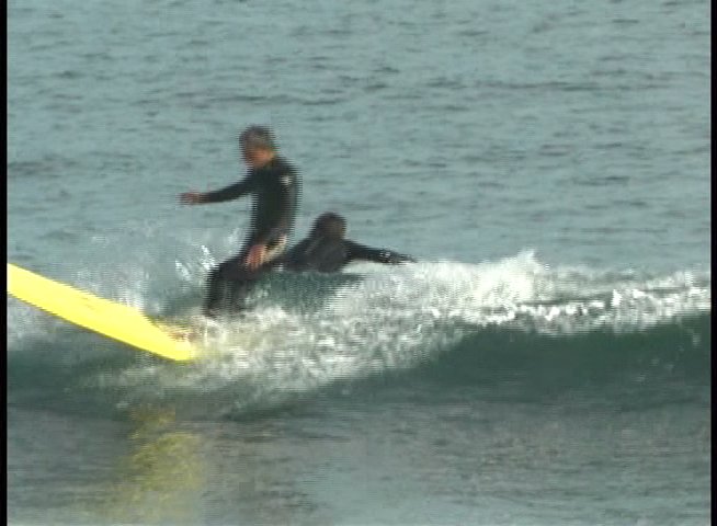 A surfer wearing a wetsuit maintains balance while navigating waves on a surfboard in an ocean setting.