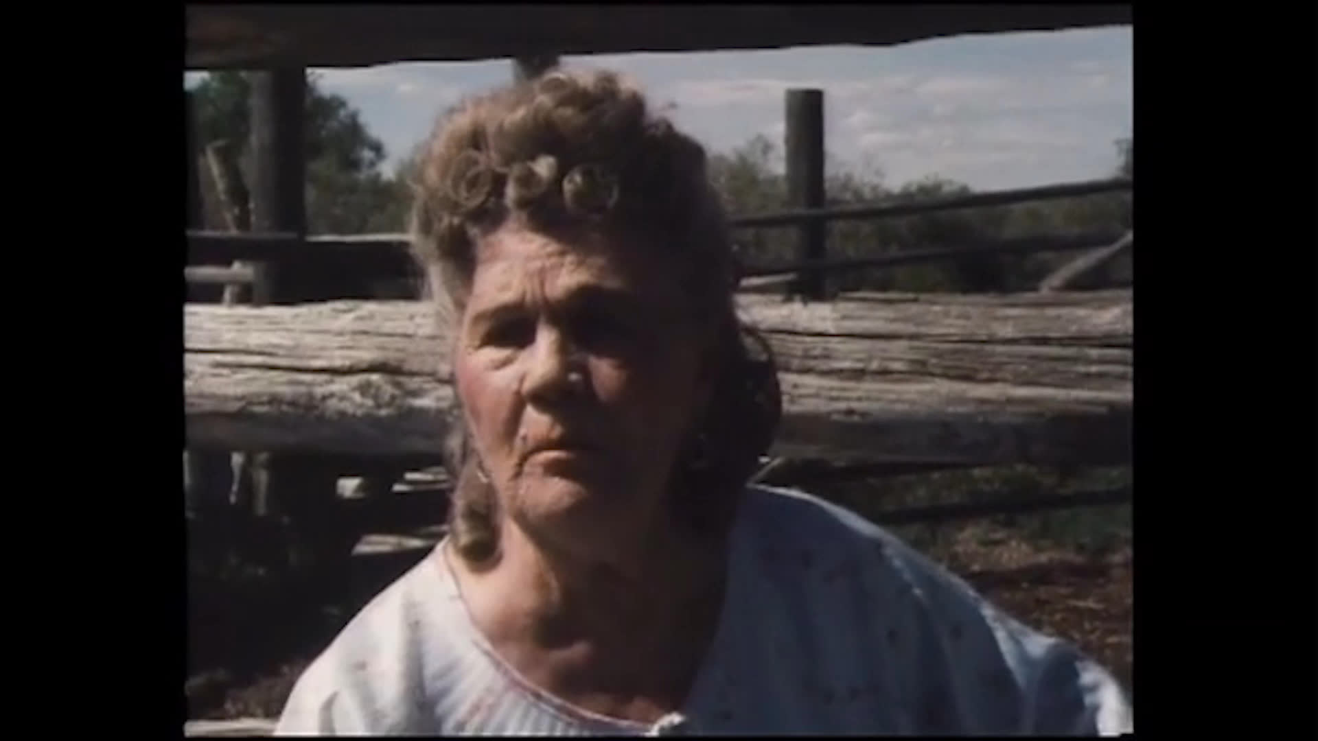 A woman stands beside a corral as another rancher describes her skill in delivering calves and treating livestock. A hay-lifting machine raises a load across the open ranch landscape.