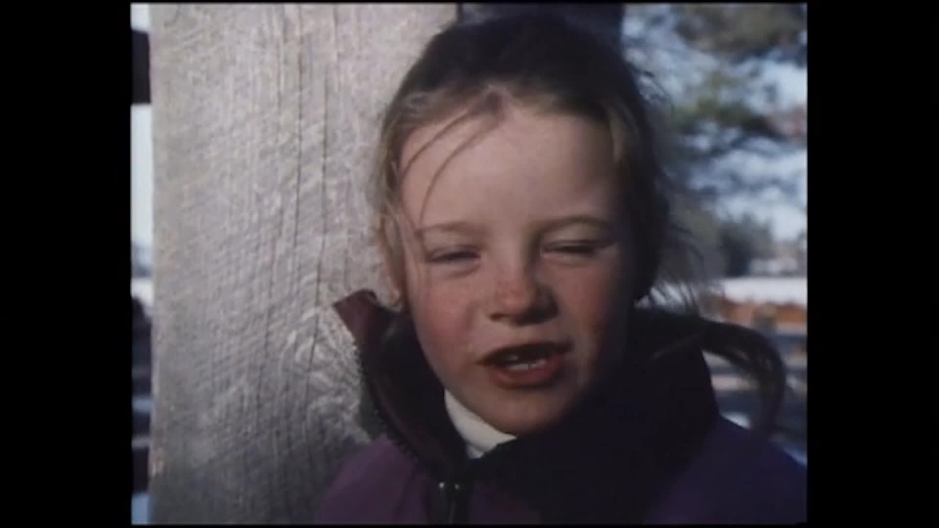 A young child in a wooden livestock corral talks about working cattle and riding all day. Their candid answers convey both enjoyment and mixed feelings about the job.