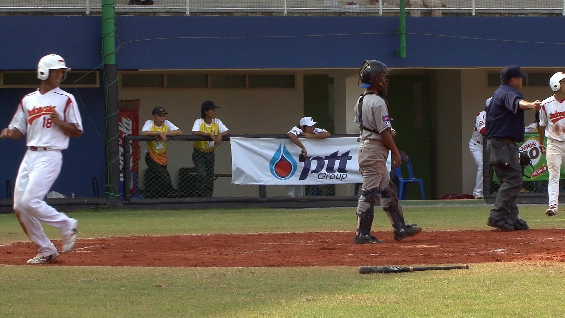 Athletes compete in a baseball match between Indonesia and Cambodia, marked by high scoring on the stadium scoreboard. Players demonstrate batting and defensive skills on the field while teammates observe from the dugout.