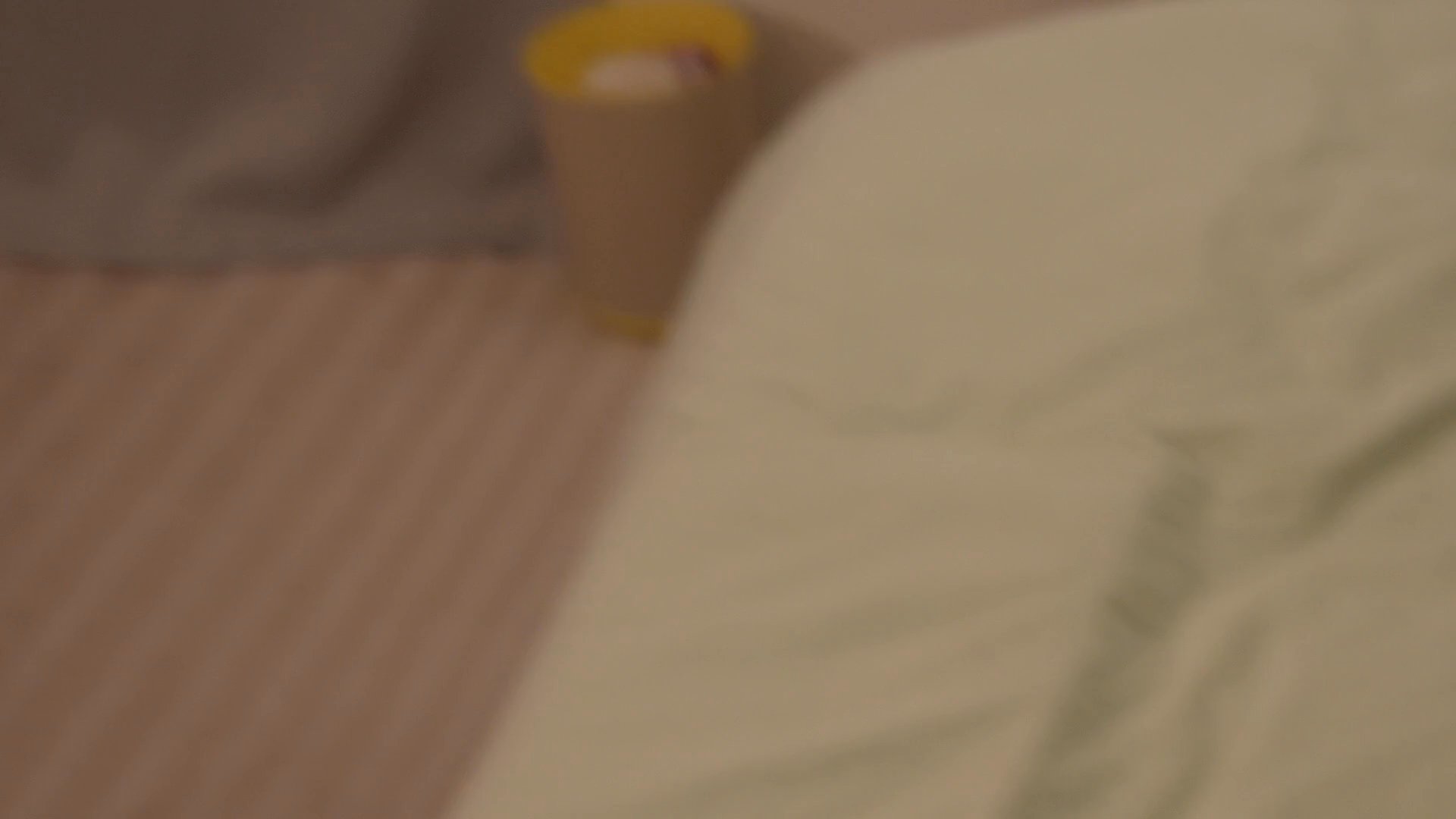 A young woman lies awake in bed, visibly distressed, before a mature woman enters the room to check on her, establishing a tense domestic atmosphere.