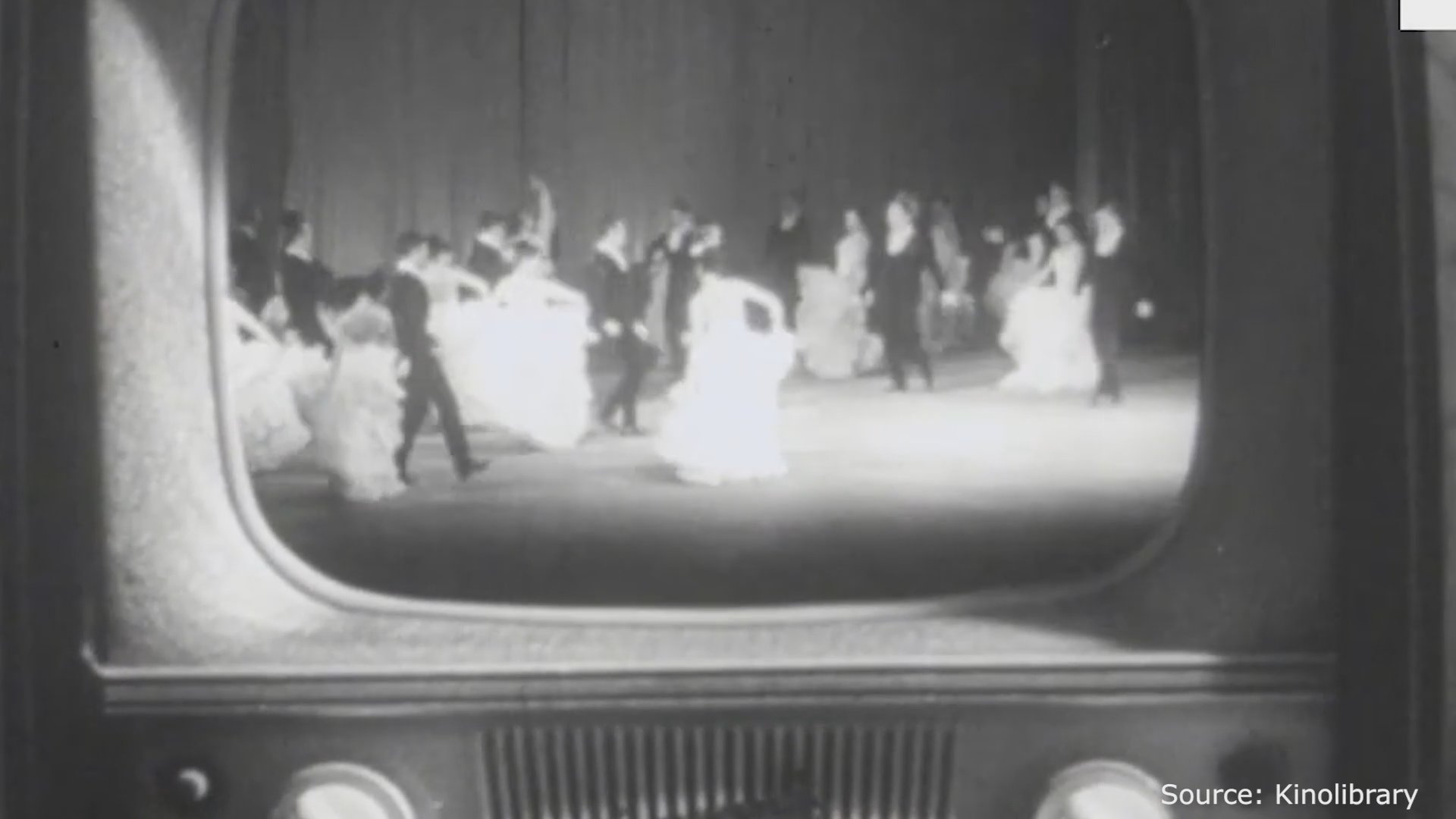 Two children watch a televised ballet performance on a vintage television set in a domestic living room setting.