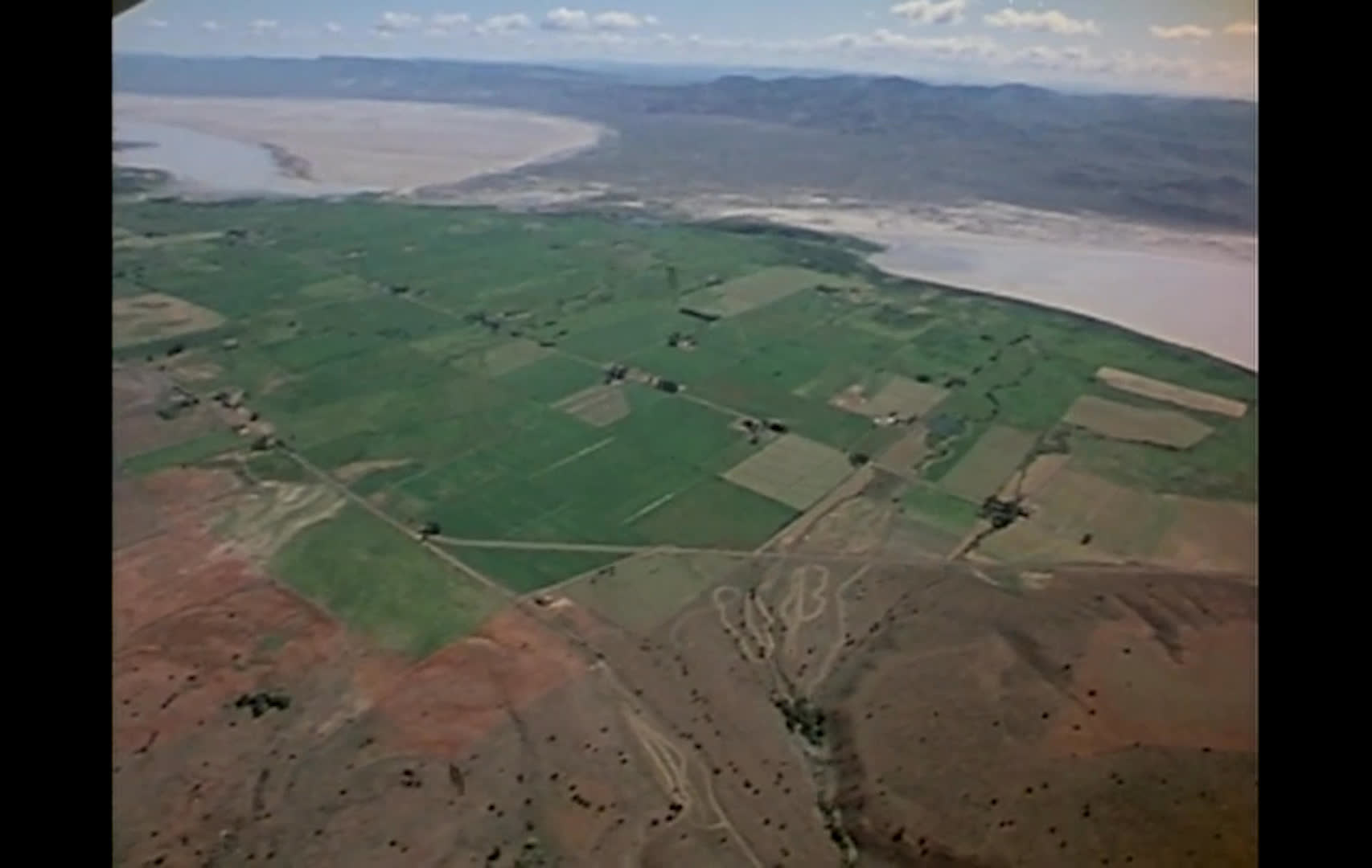 Aerial views contrast green, cultivated hay fields with the dry, scrub-covered public range surrounding them. The narration explains how ranchers graze cattle on public lands to reserve private acreage for winter hay.