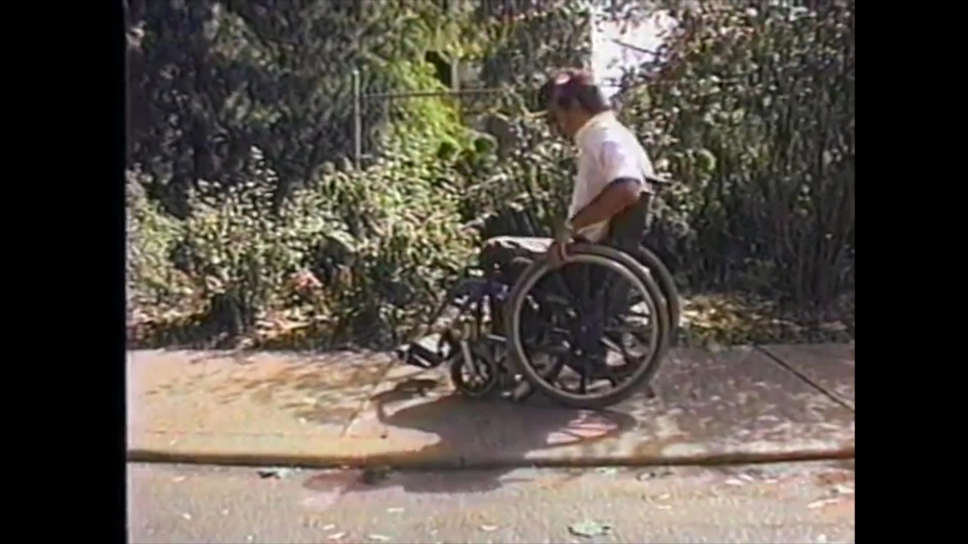 An individual demonstrates the process of transferring into a wheelchair on an outdoor walkway, followed by a professional conversation with an employee inside a retail store.