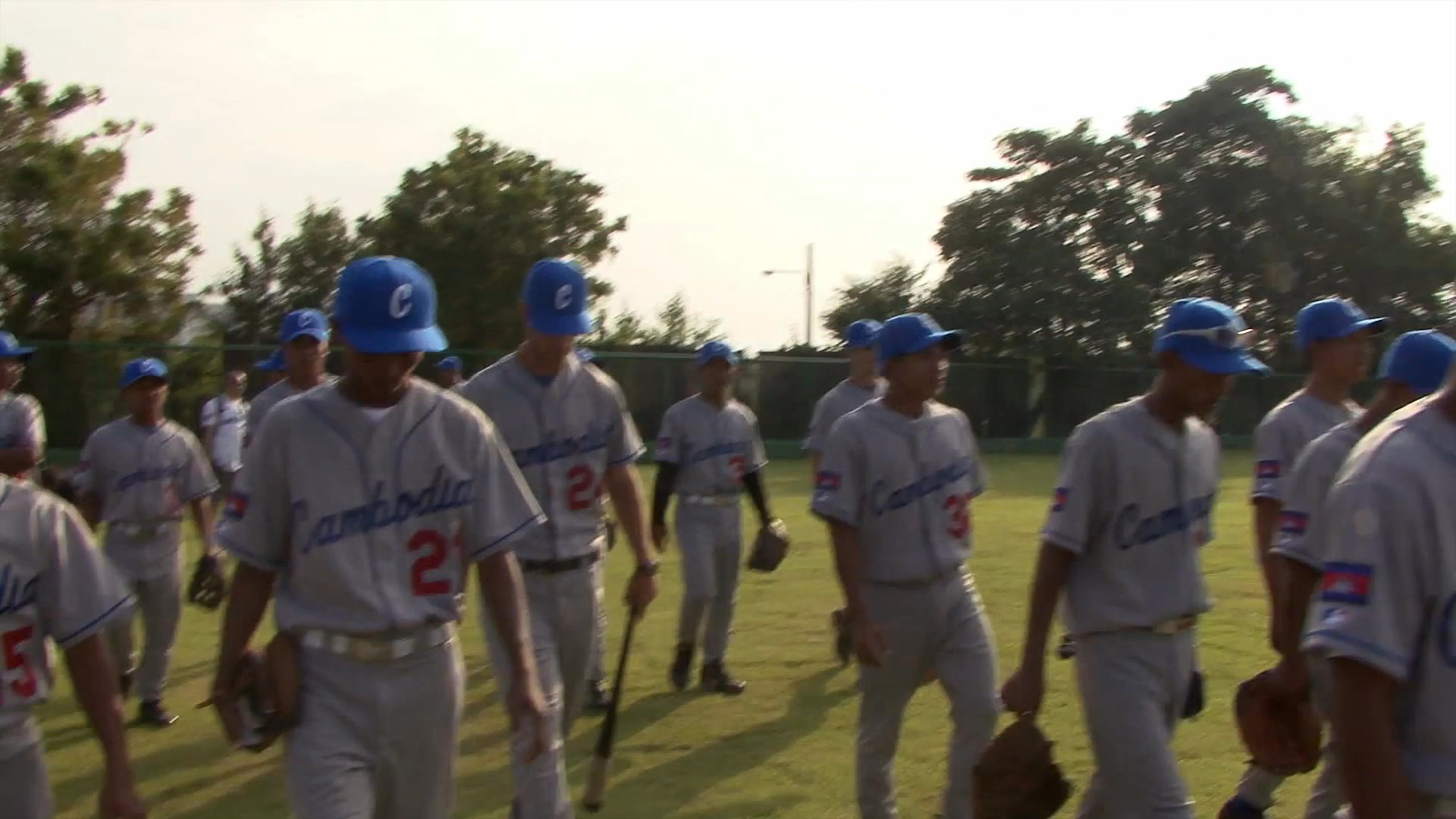 Players and staff of the Cambodia national baseball team gather on the field during an outdoor training session.