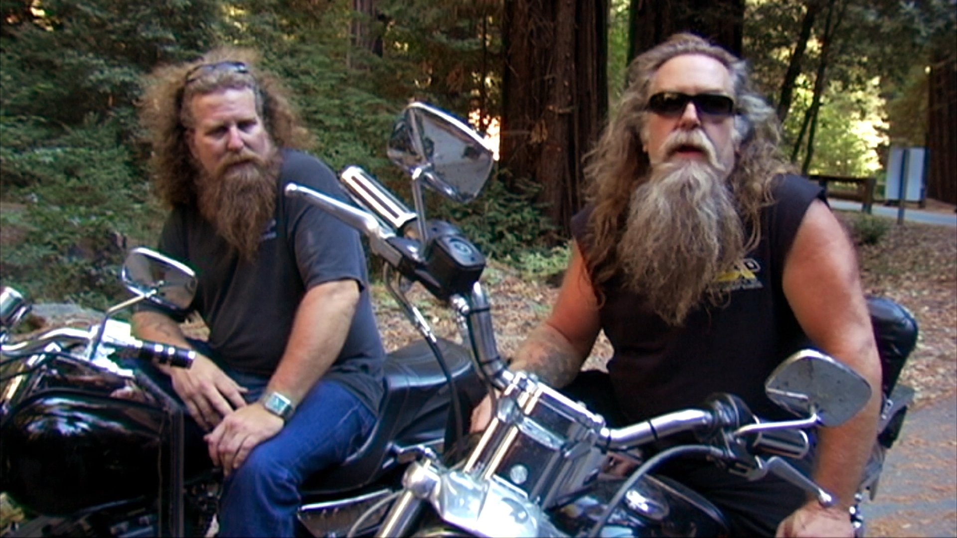 An elderly woman and a bearded motorcyclist share individual reflections during separate outdoor interviews set against a forest backdrop.