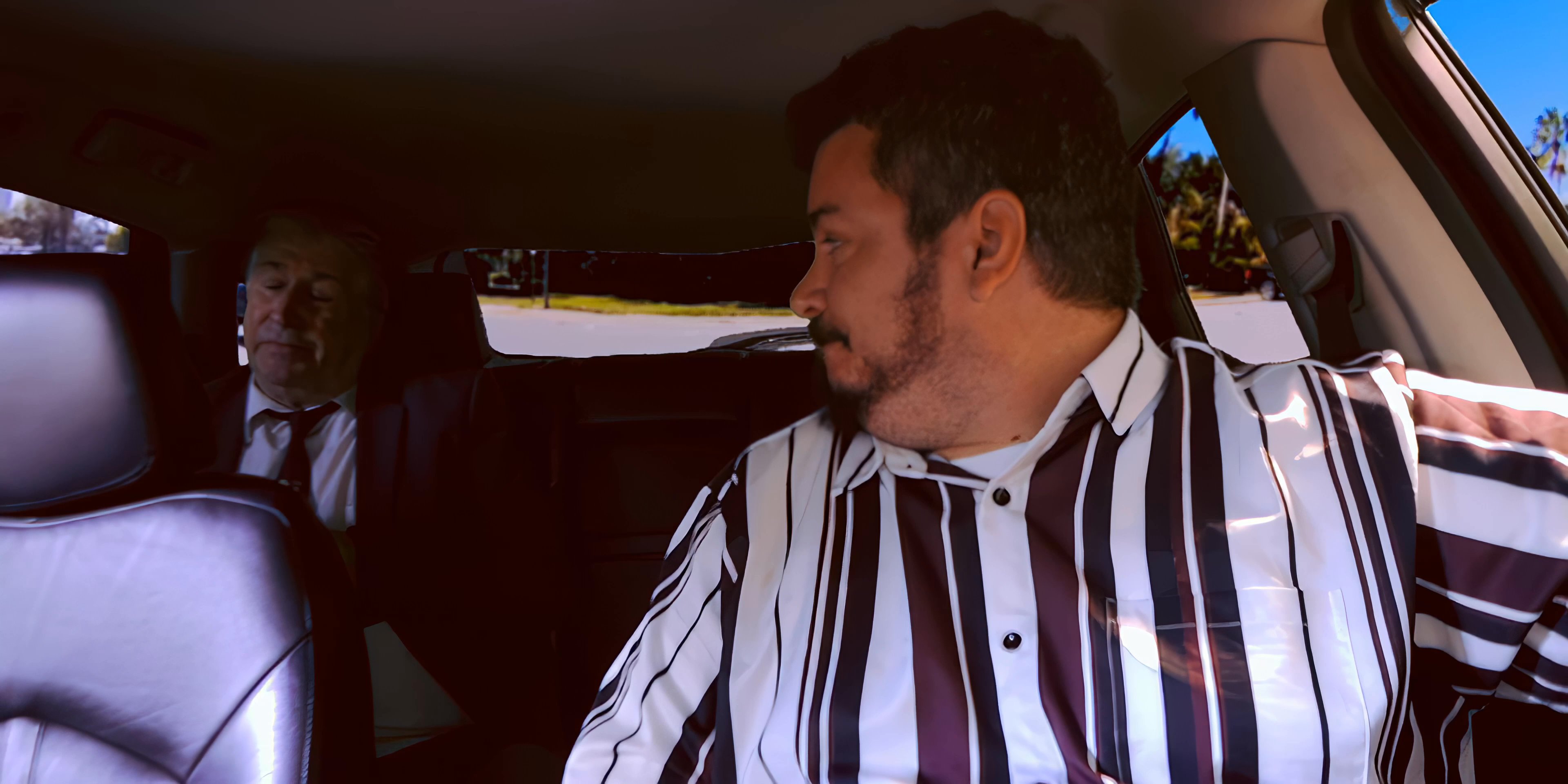 A man in a striped shirt engages in a conversation while driving through an urban environment. The perspective shifts from the vehicle's interior to an aerial view of a city skyline.