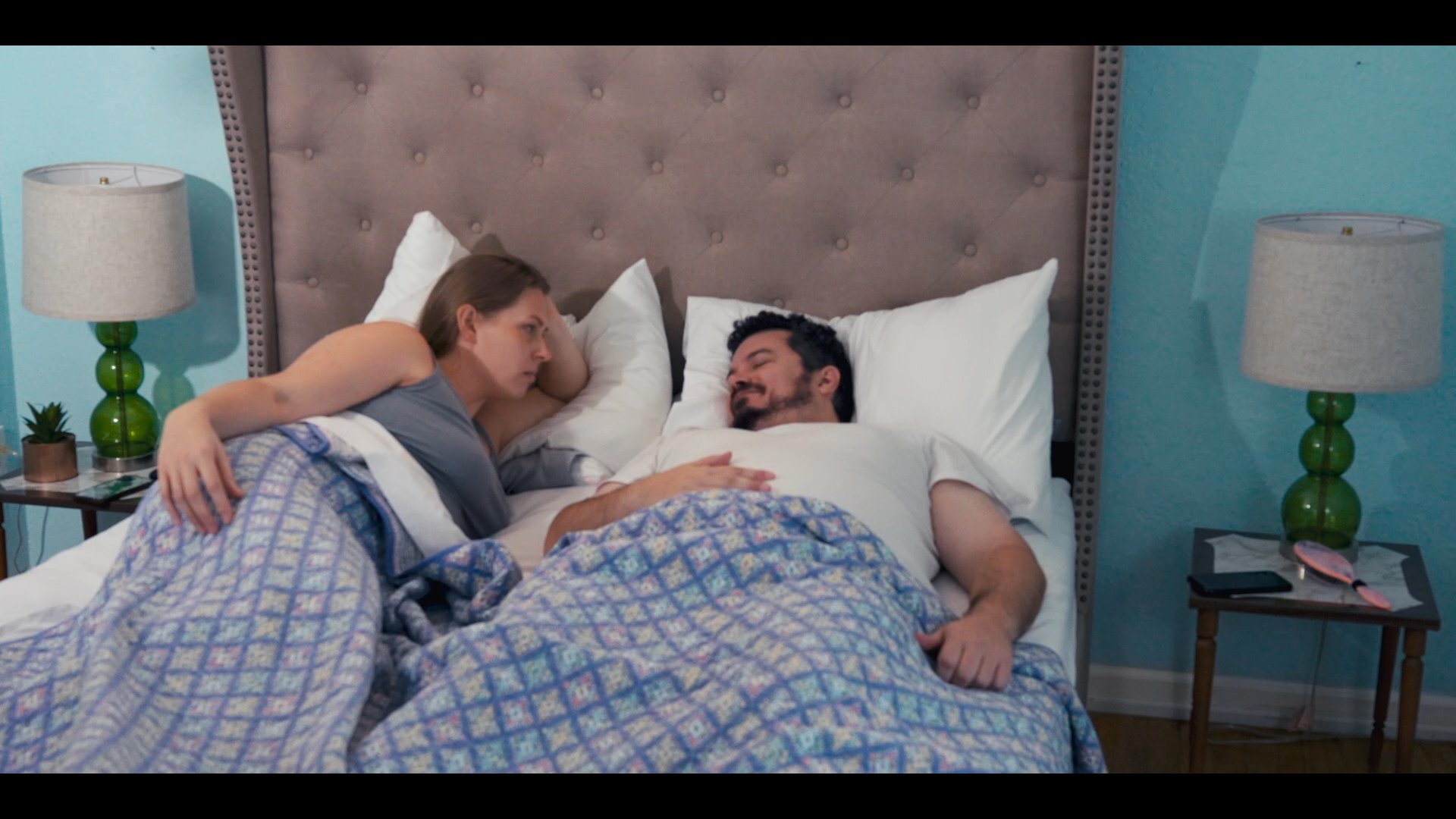 A man and a woman engage in a quiet conversation while resting in bed before the man rises to start his day.